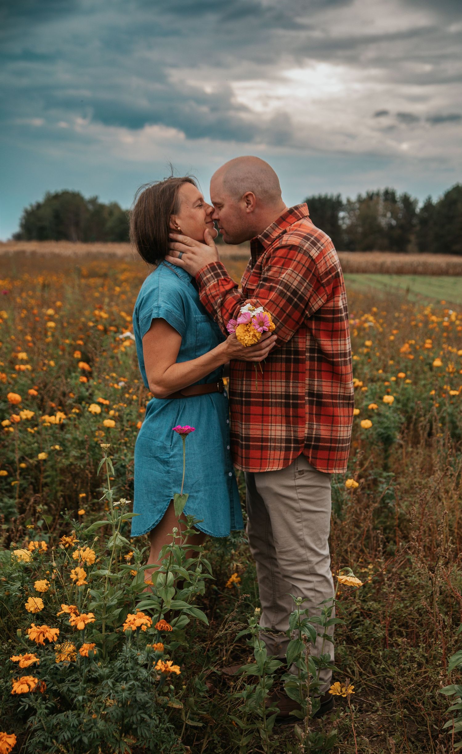 A couple shares a romantic moment in a field of blooming yellow wildflowers under moody cloudy skies.