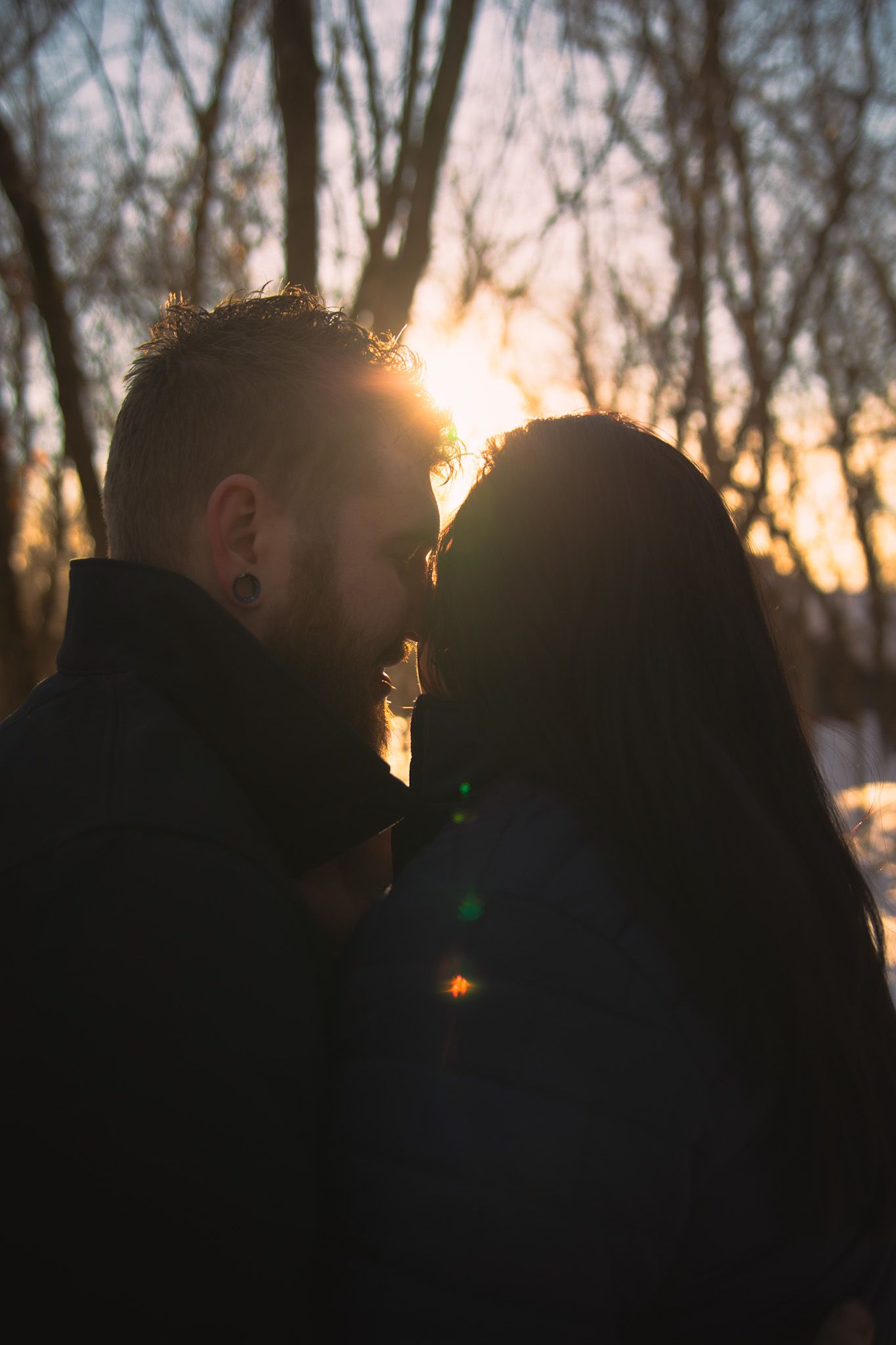 Silhouetted figures stand against a winter sunset with bare trees in the background, creating a dramatic backlit scene.