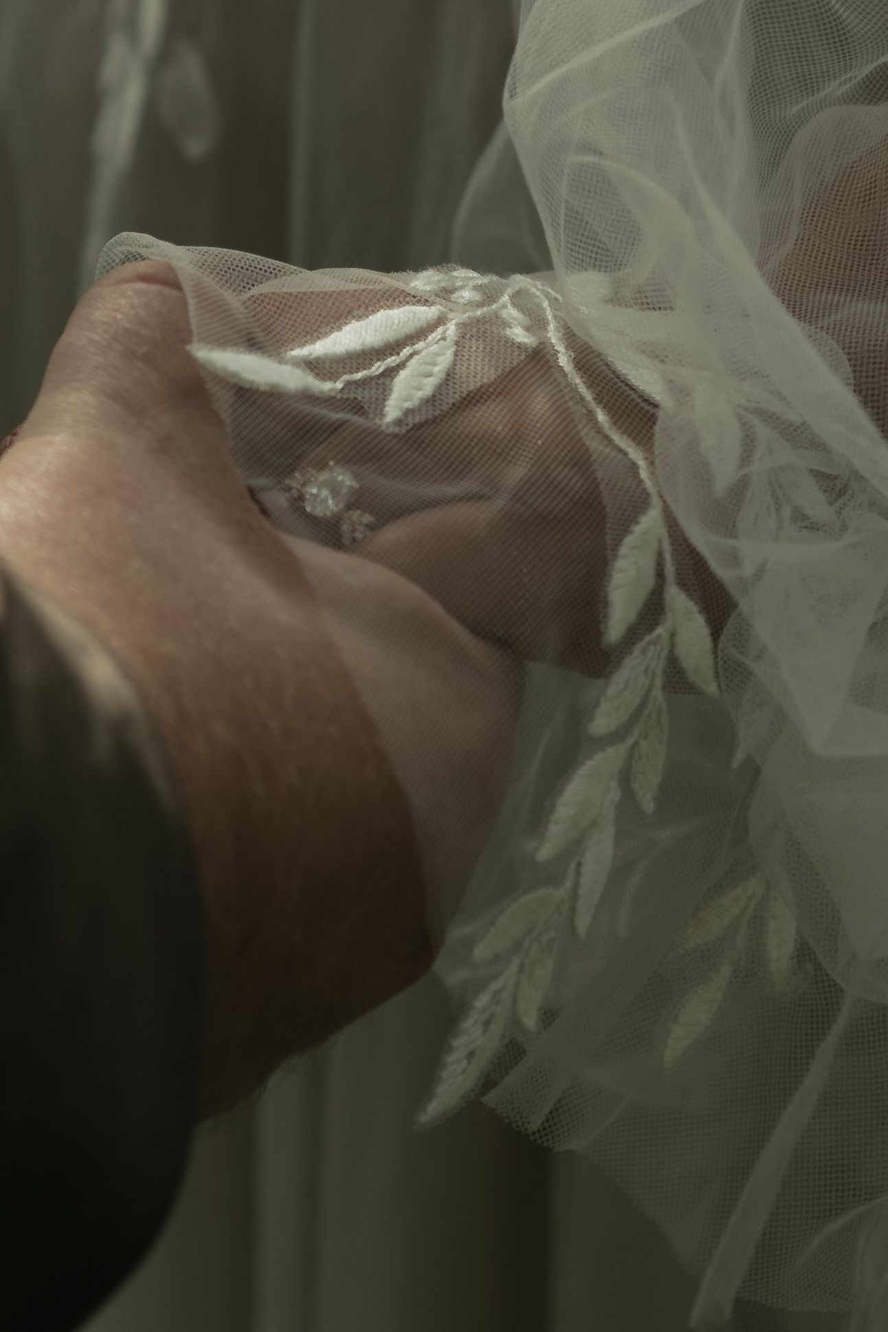 Close-up of hands holding delicate white lace wedding veil with floral embroidery details.