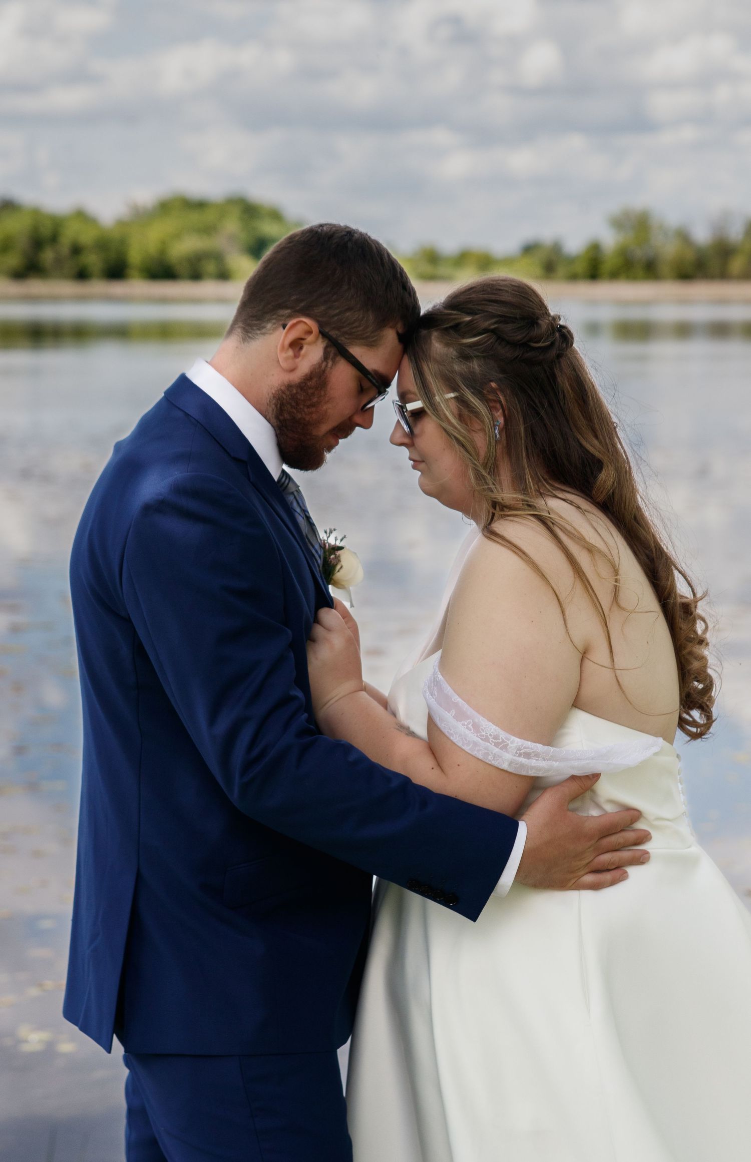 Romantic wedding couple embraces outdoors by a serene lake on their special day.