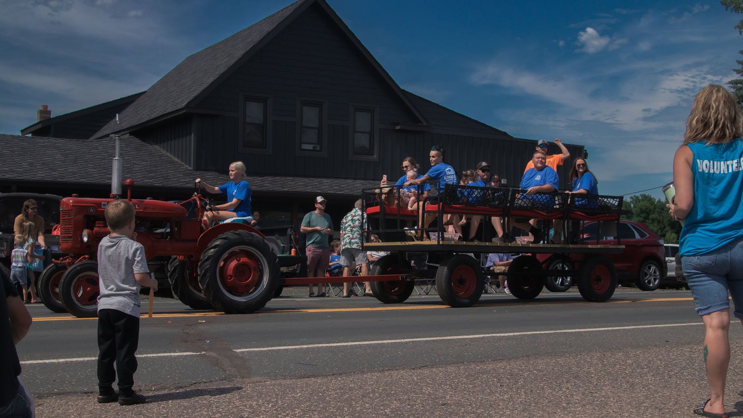 Wide angle shot of vintage automobiles lined up at a car show against dark buildings and blue sky.
