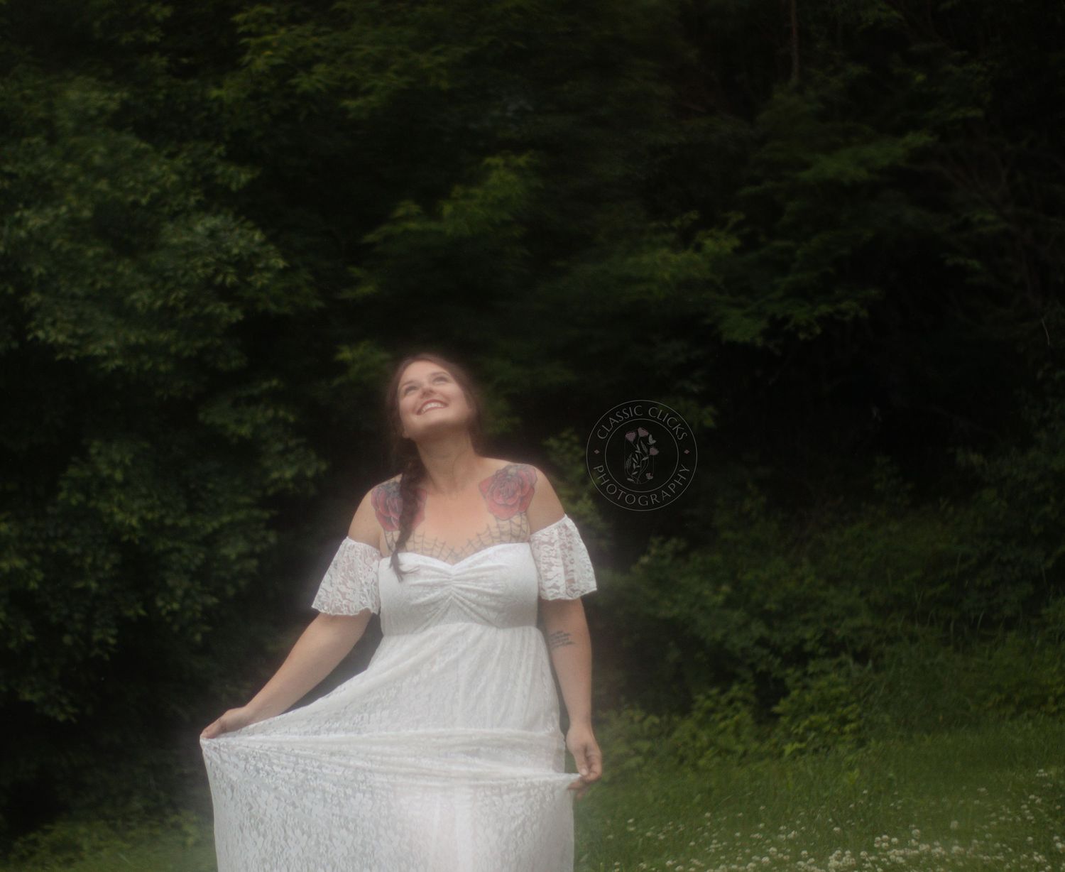 A woman in a white dress poses joyfully in a meadow surrounded by dark forest.