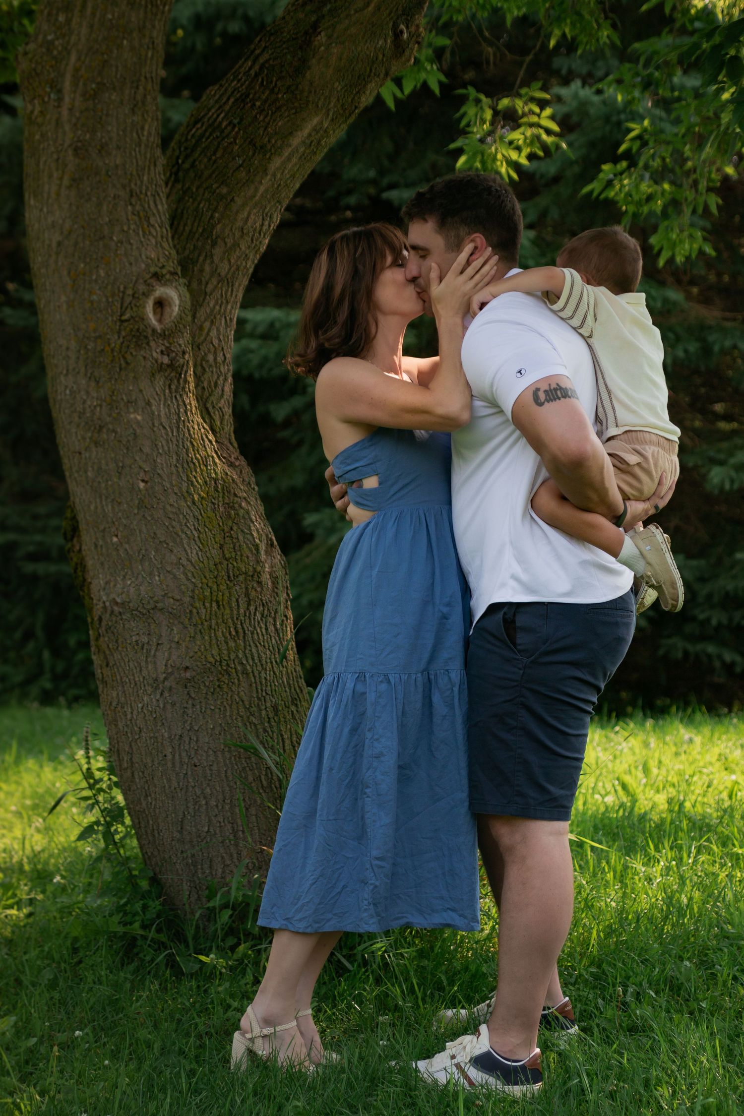 Sweet couple embraces tenderly under a leafy green tree on a sunny summer day.