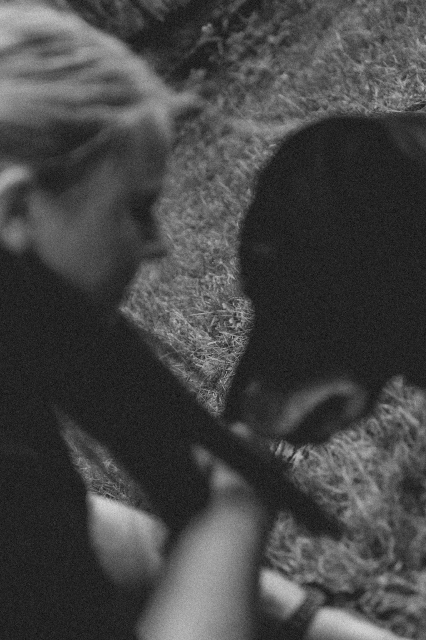 Black and white photo of two people bending over grass, captured in a candid, blurred artistic style.