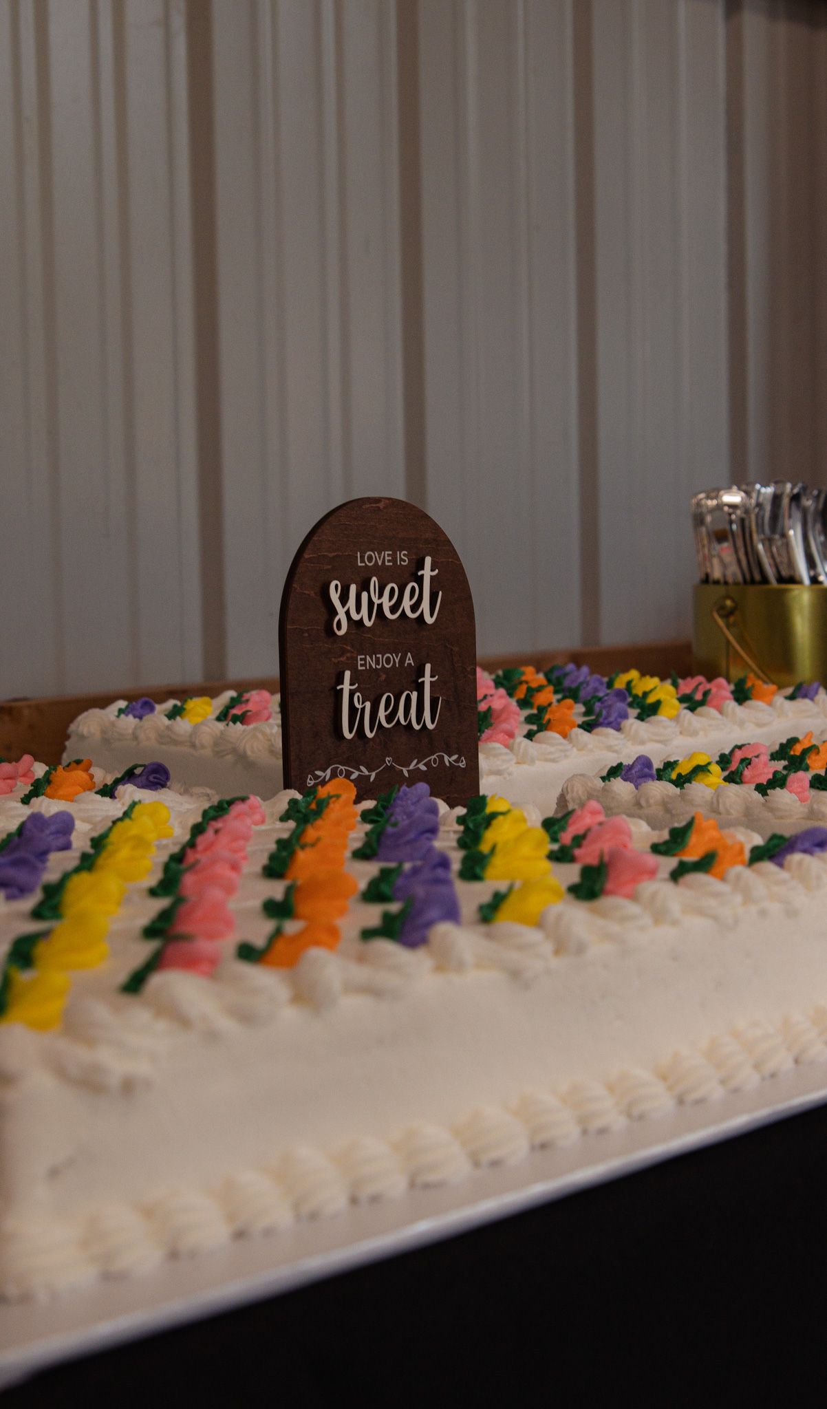 A white frosted cake decorated with colorful buttercream rosettes in yellow, orange, pink and purple along the top edge.