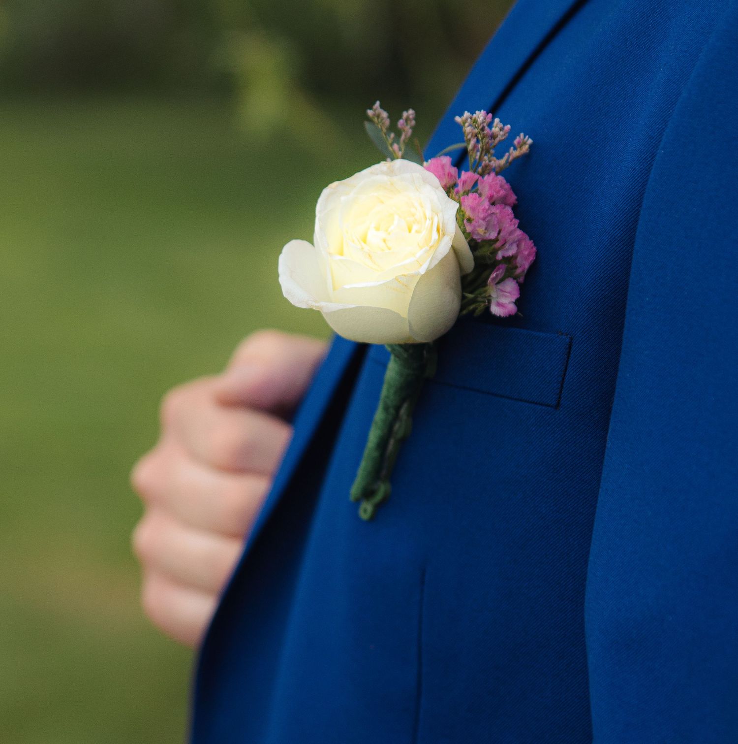 Close-up of a white rose and purple flower boutonniere pinned on a navy blue suit lapel.