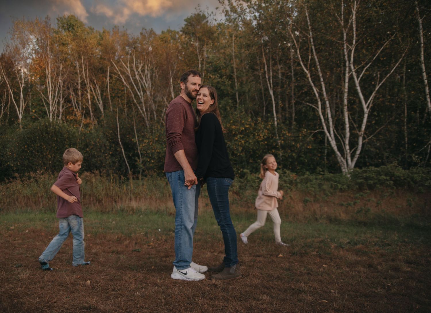 A family walks together through a scenic autumn forest path during golden hour sunset.