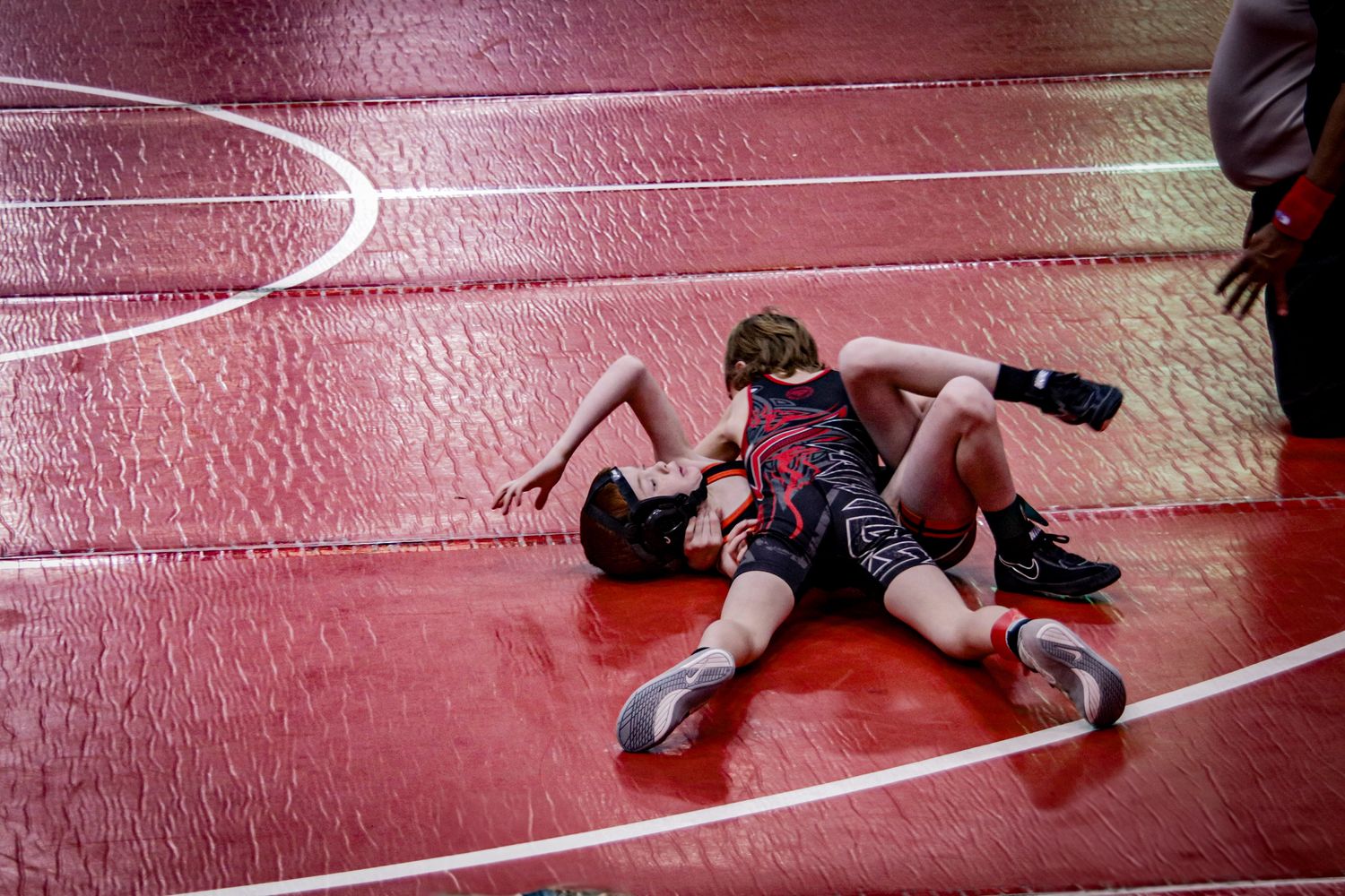 A sequence of wrestling moves being performed on a red wrestling mat during a competitive match.