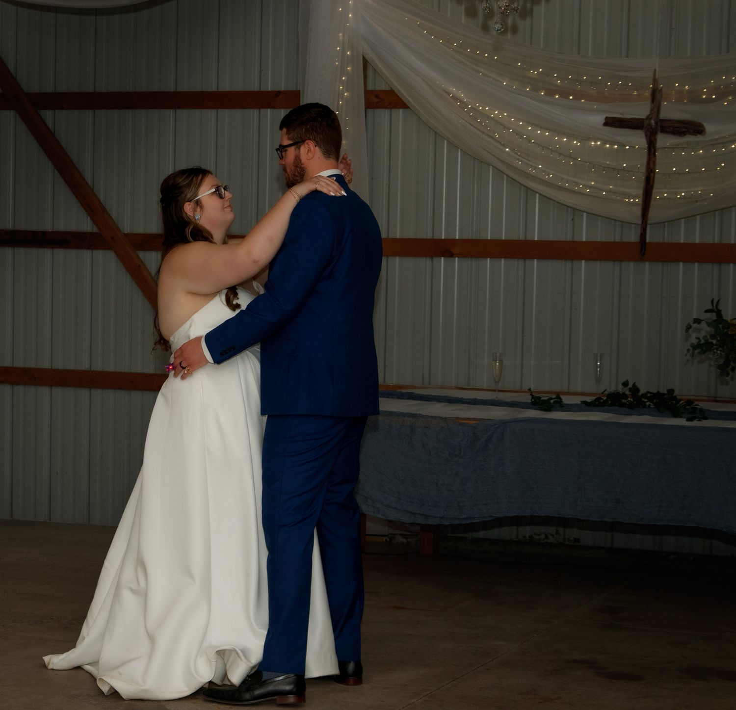 A couple dancing intimately in a rustic barn venue decorated with romantic string lights and draping.