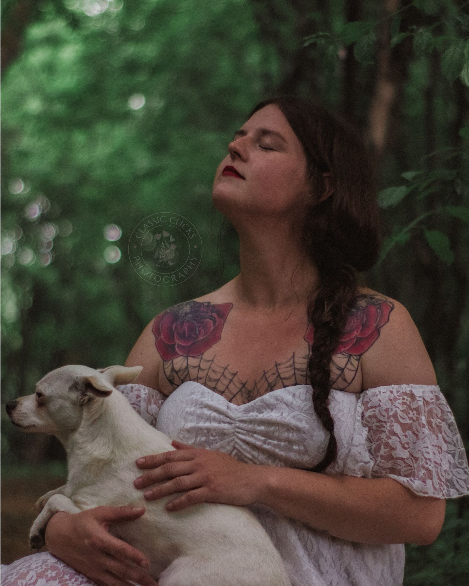 A person in a white lace dress holds a small white lamb while standing in a dreamy forest setting.