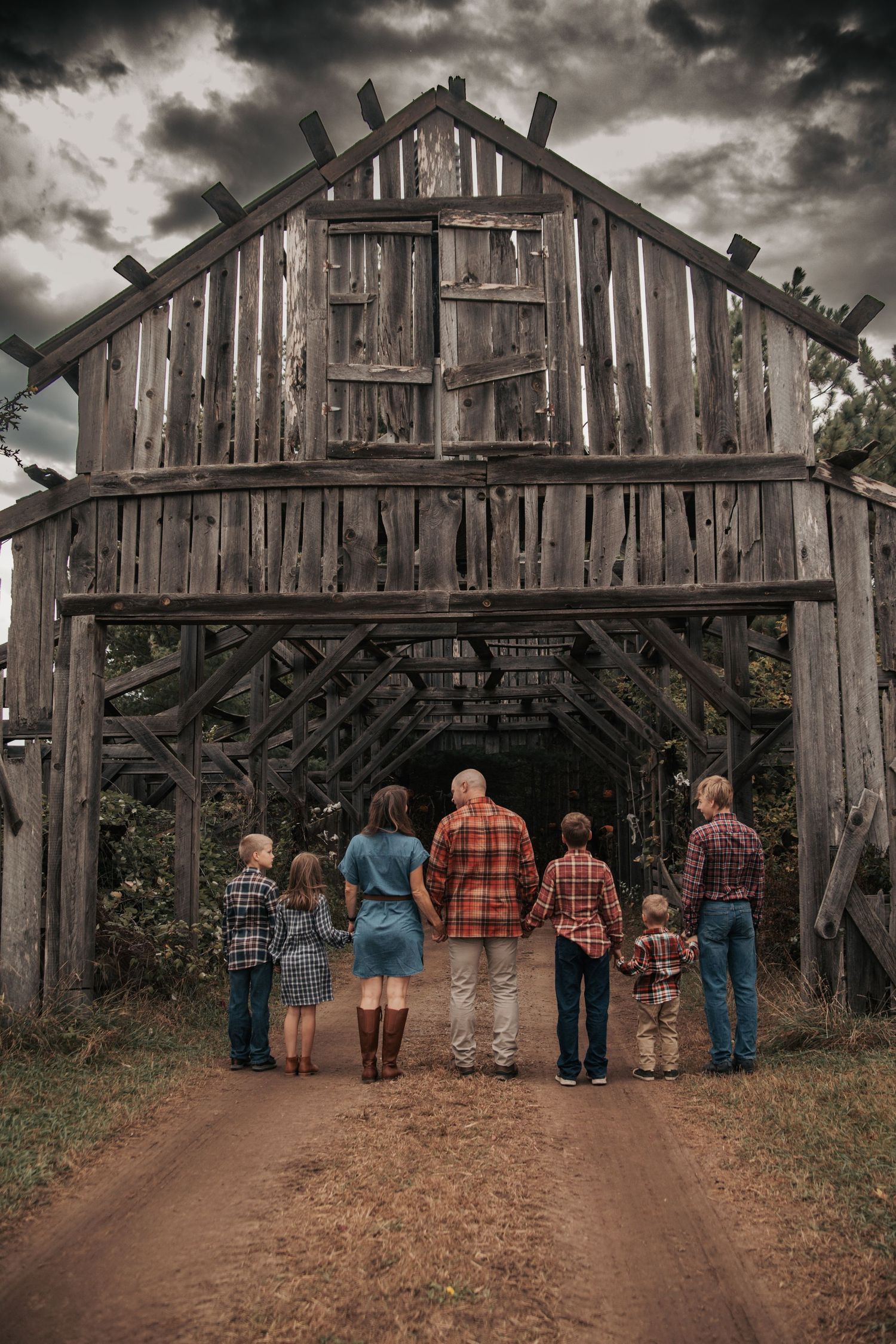 A group stands in front of a rustic wooden barn under dramatic stormy skies wearing plaid shirts.