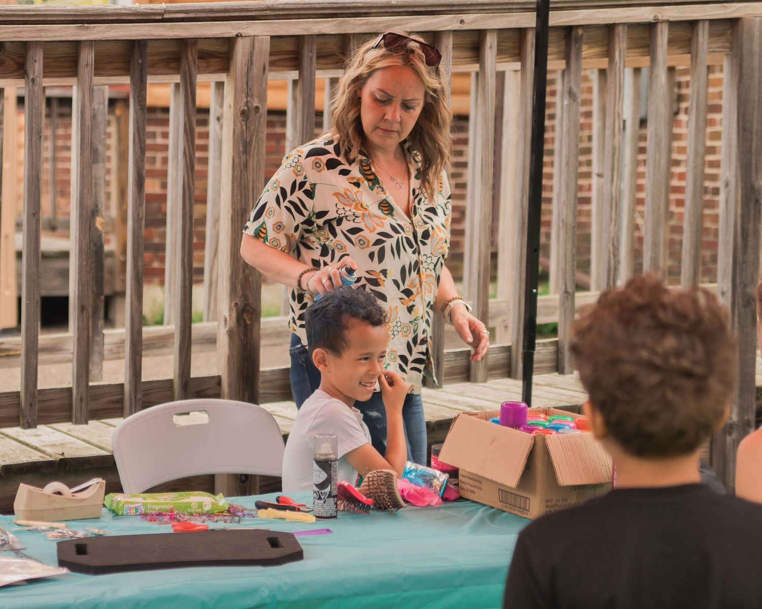 People gathered around a wooden deck table with colorful items spread out.