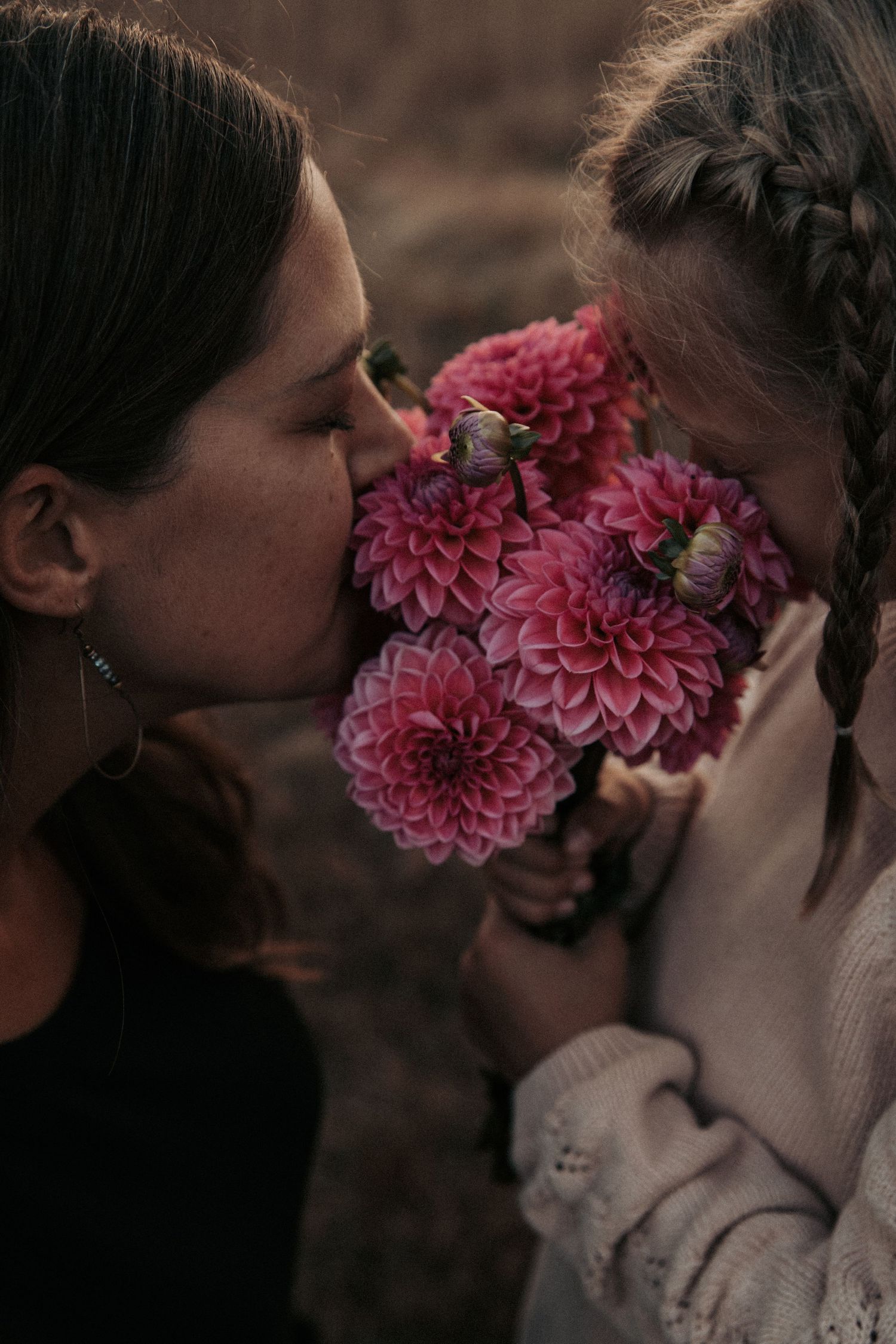 Two people share an intimate moment smelling pink dahlia flowers together in a moody atmospheric setting.