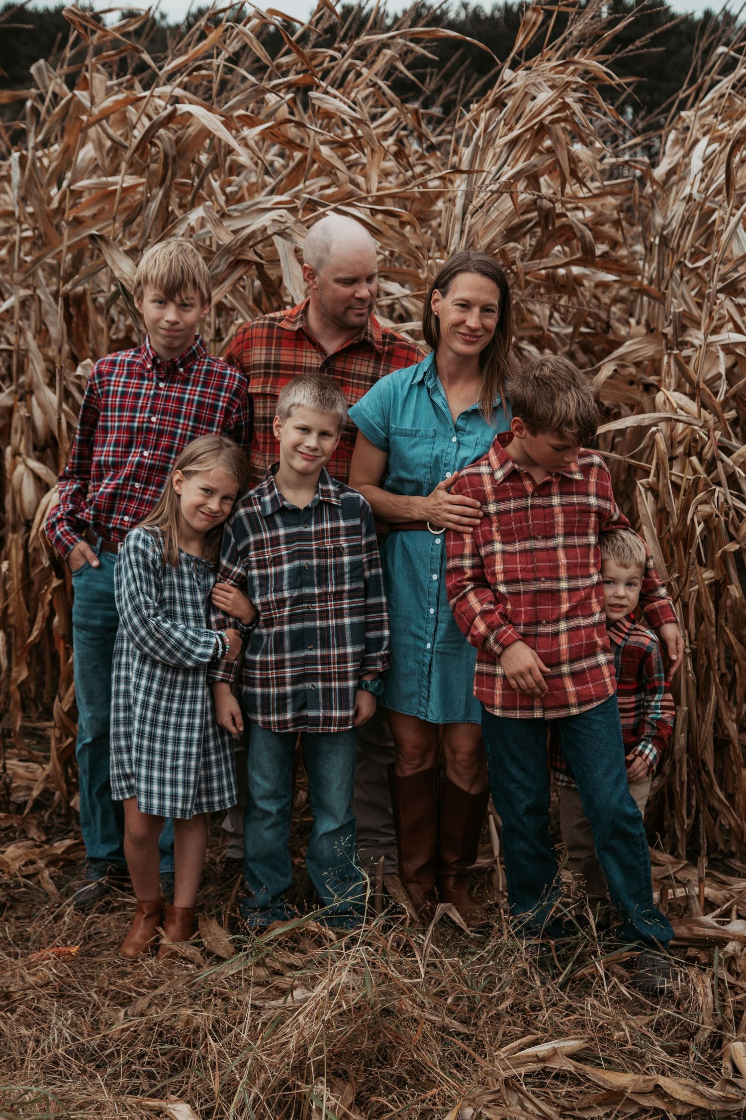 A playful group poses together in a cornfield during autumn wearing plaid and casual clothing.