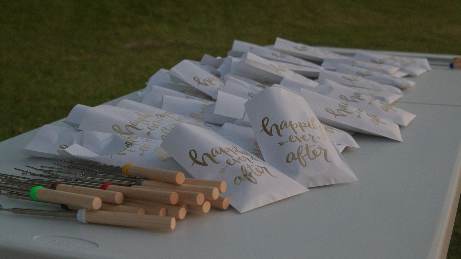 Wedding favor bags and pencils arranged neatly on a white table at an outdoor reception.