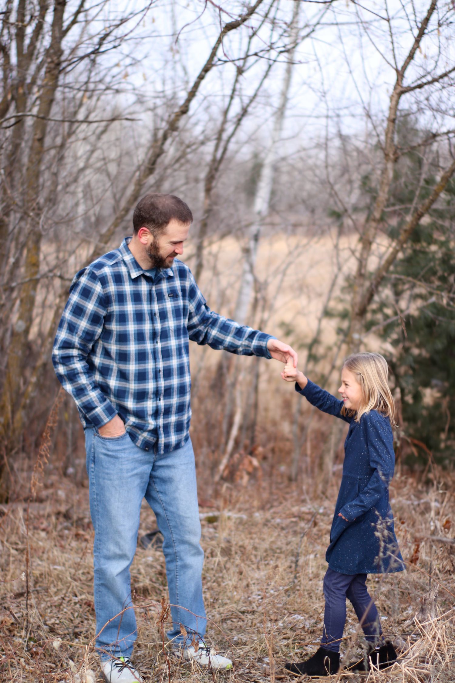 A person in plaid shirt holds hands with a small child in the woods.