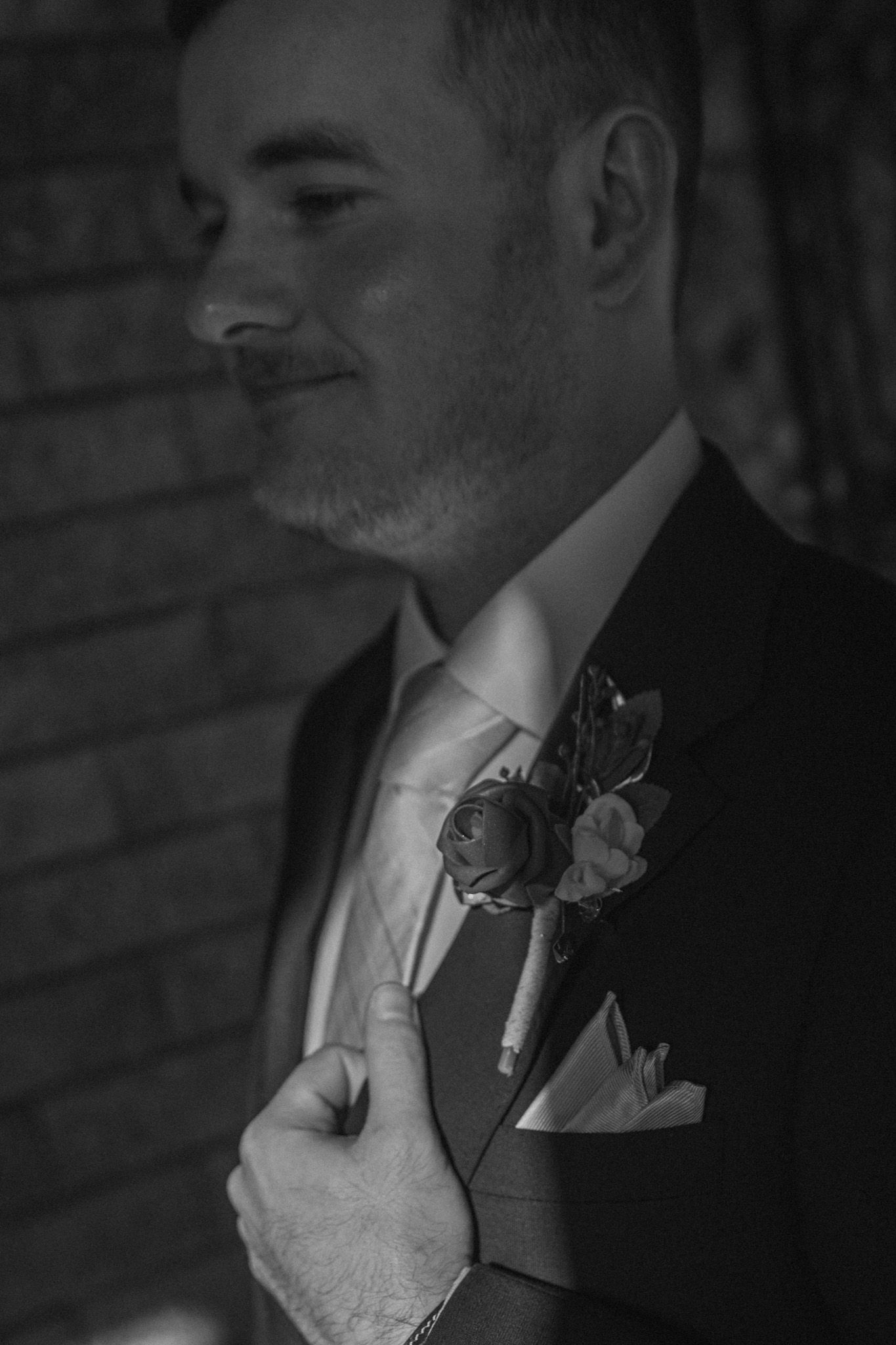 Black and white profile shot of a groom wearing a boutonniere and formal suit at a wedding.