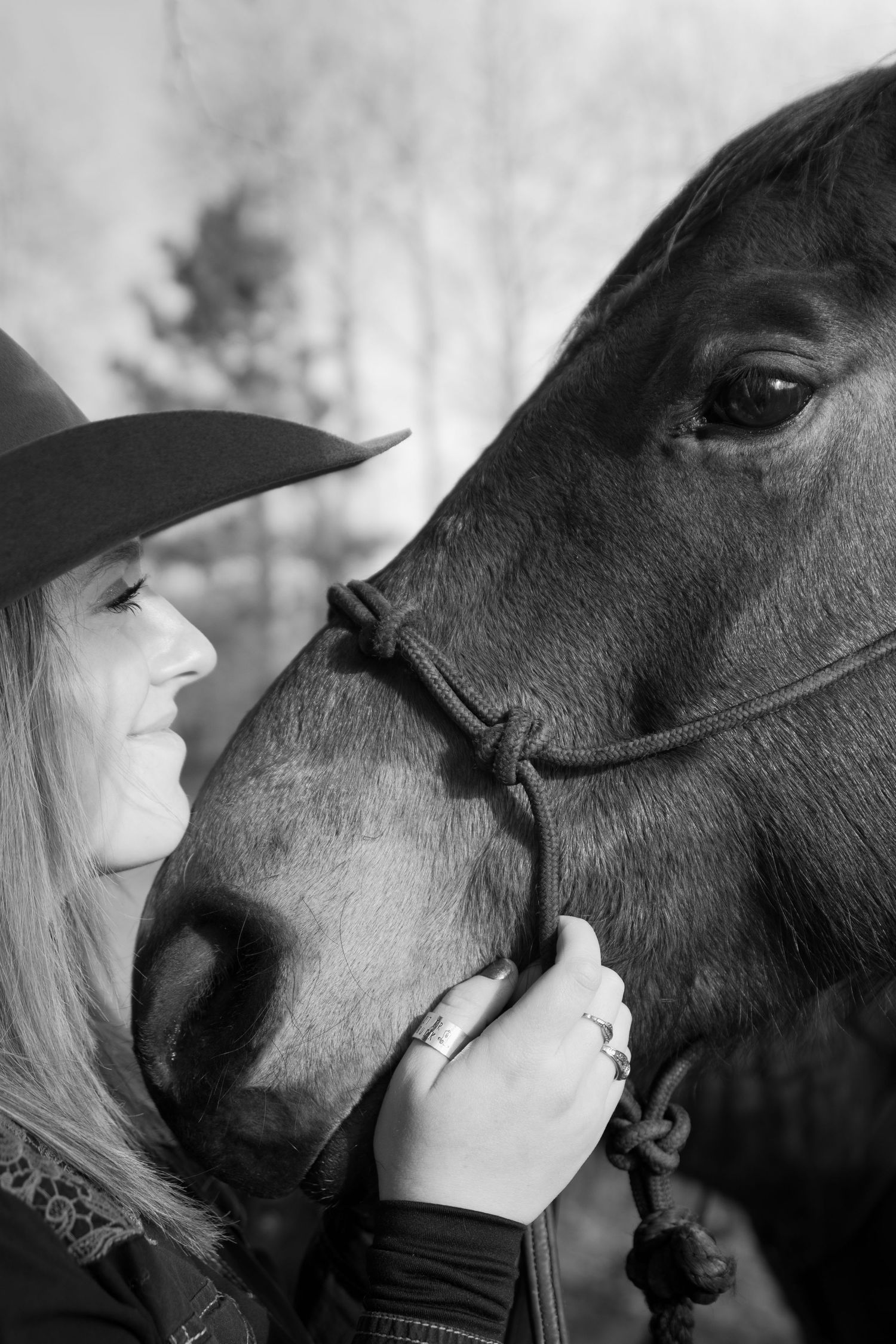 A tender black and white moment between a cowgirl in a hat and her dark horse as they share a close connection.
