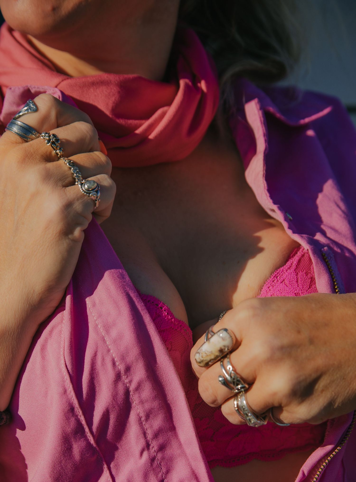 Close-up view of hands wearing multiple silver rings against pink and purple fabric background.