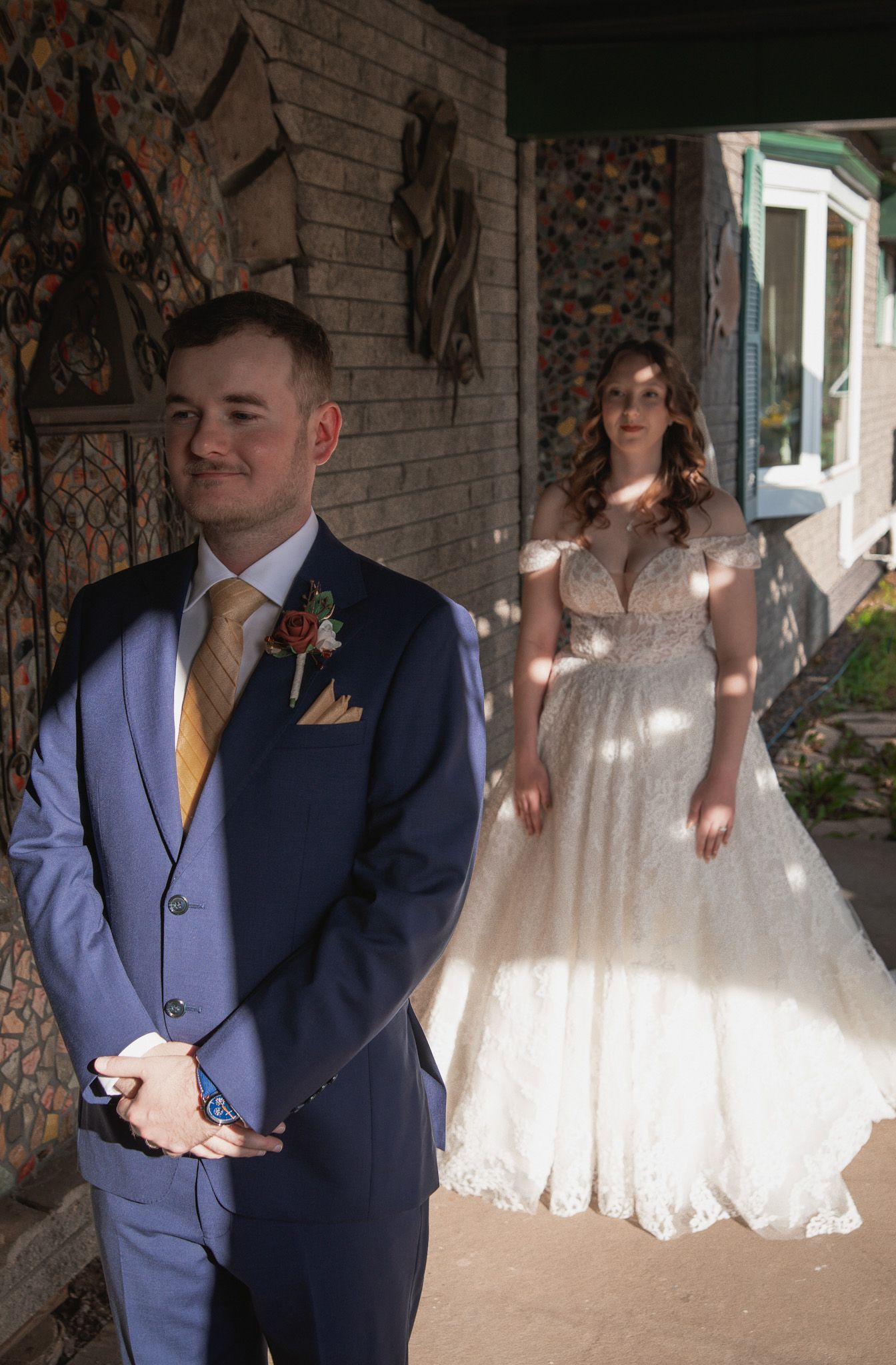 A wedding couple poses together under a brick archway in elegant navy and white attire.