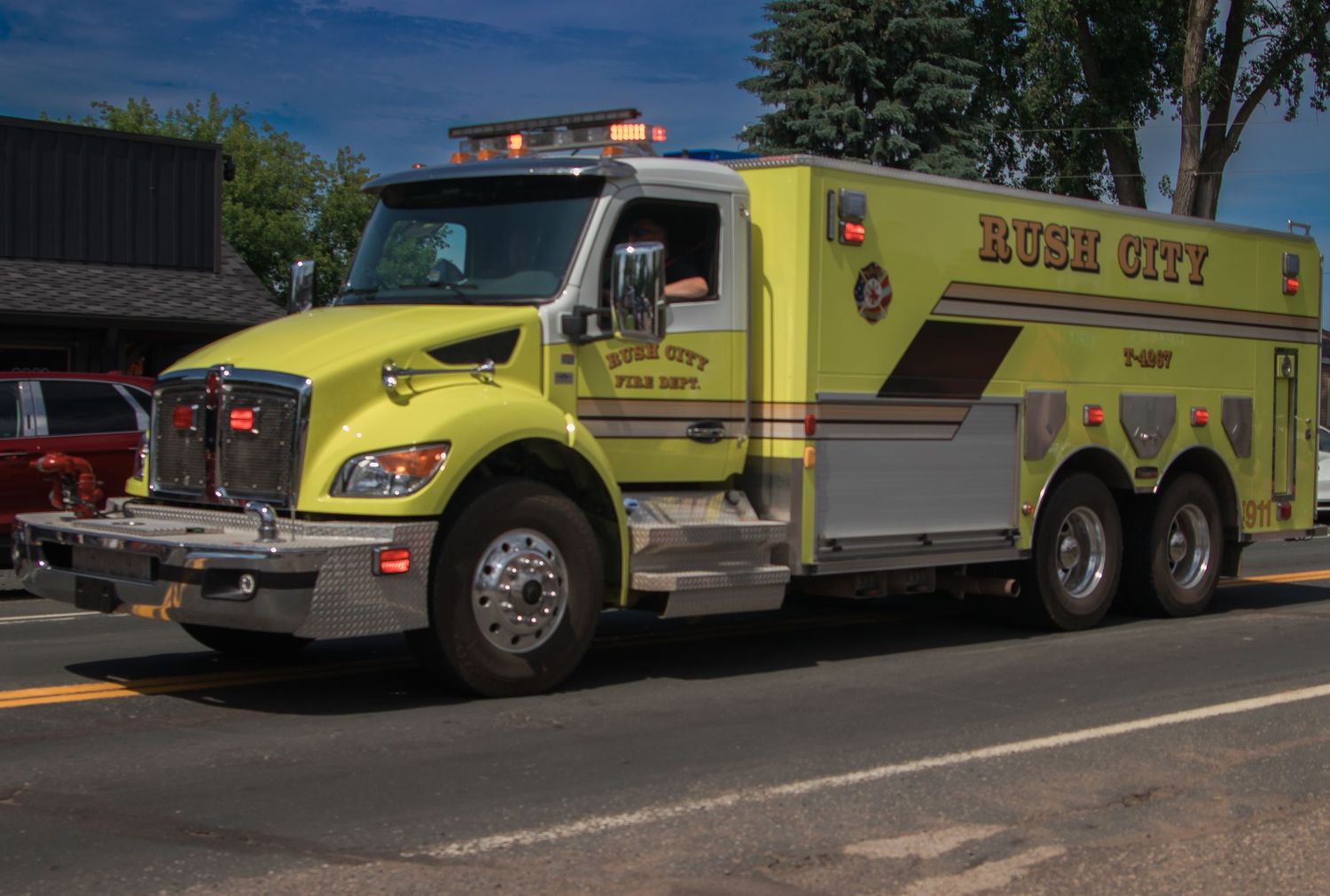 A line of yellow emergency response vehicles parked along a road against a blue sky and trees.