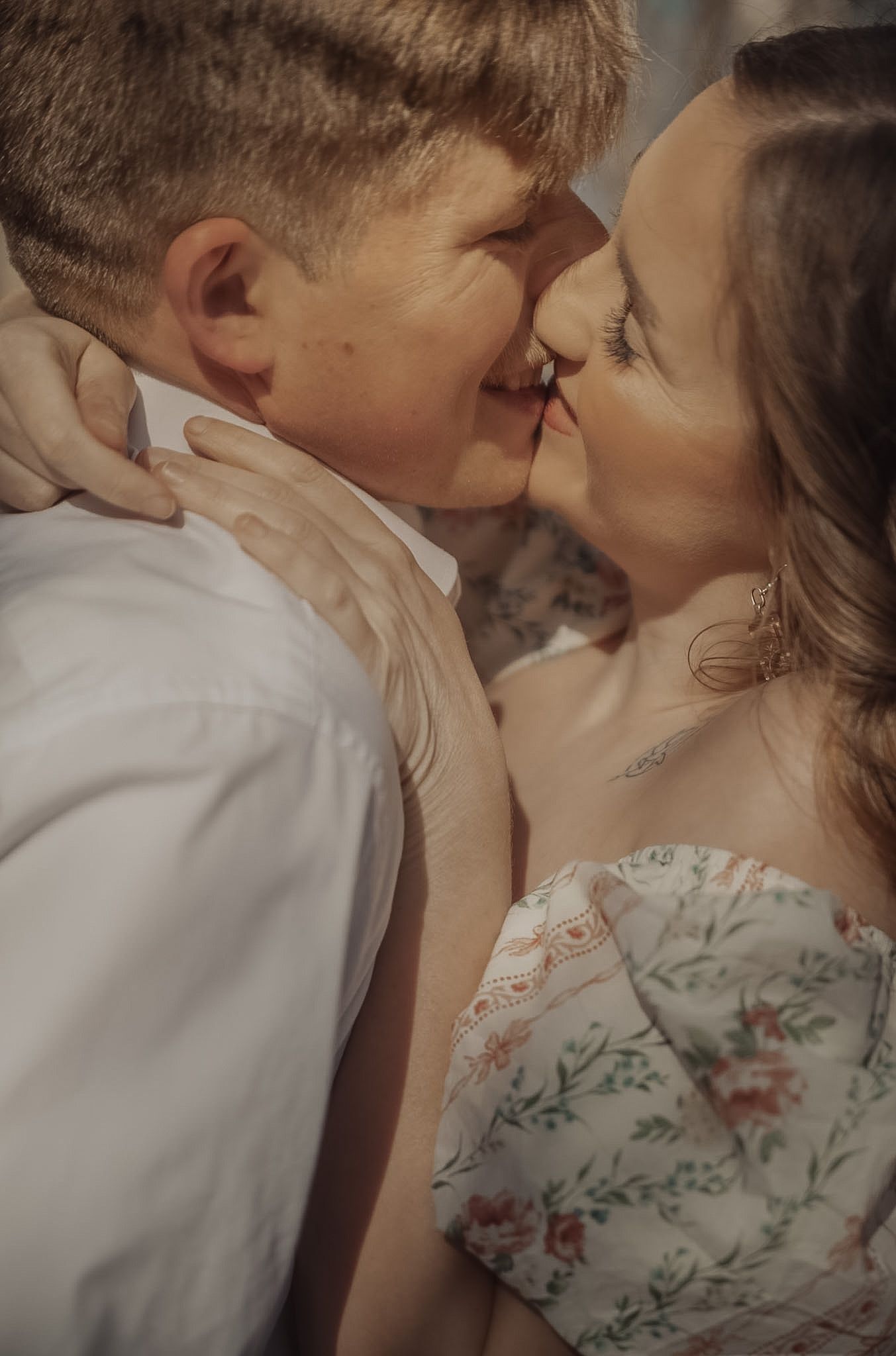 A young couple shares a romantic almost-kiss moment, smiling closely together in soft warm tones.
