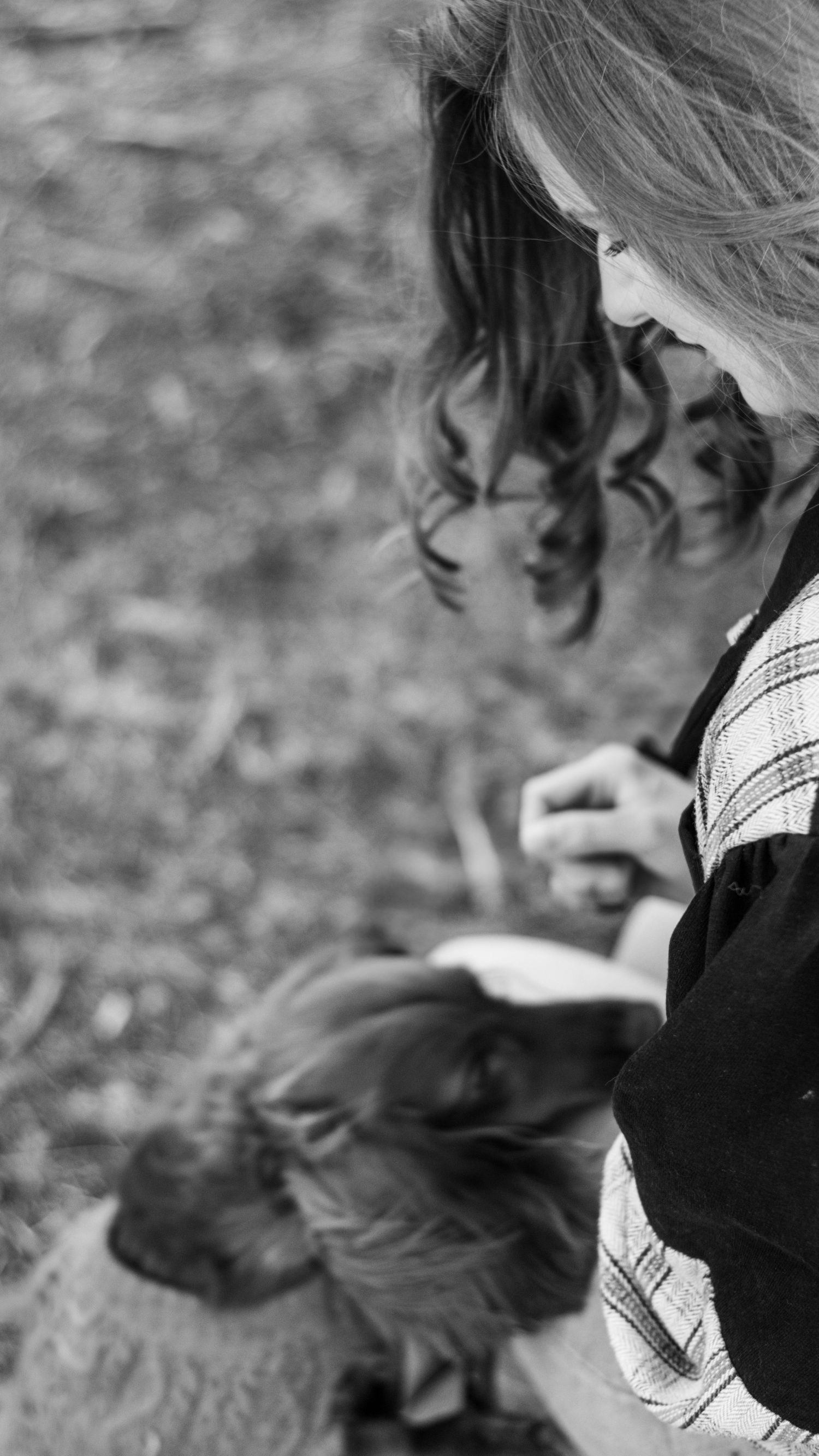 Black and white photo of a girl reading a book outdoors while a dachshund dog rests in her lap.