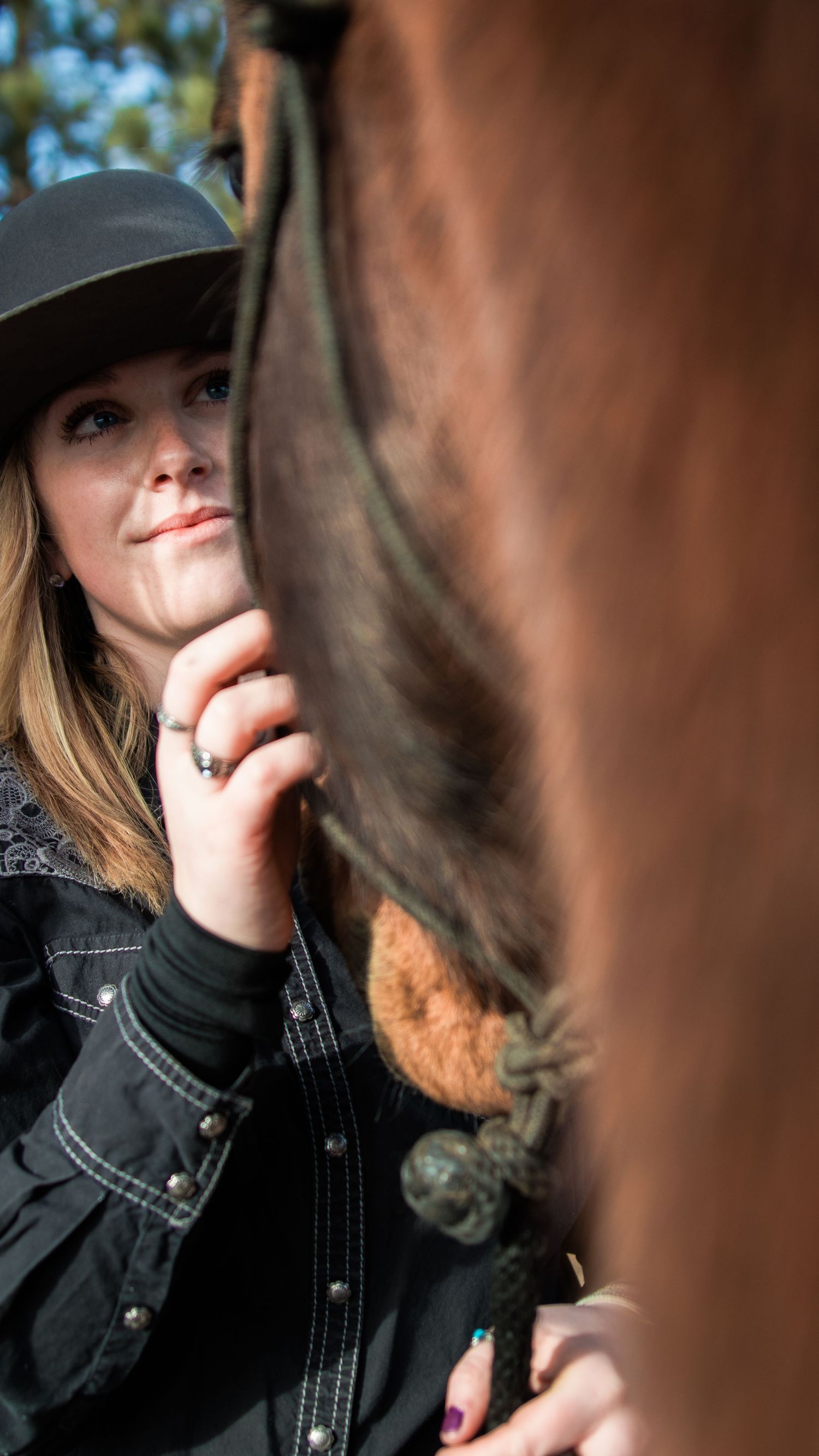 Close-up portrait of a person in a black hat with a horse's mane visible in the foreground.