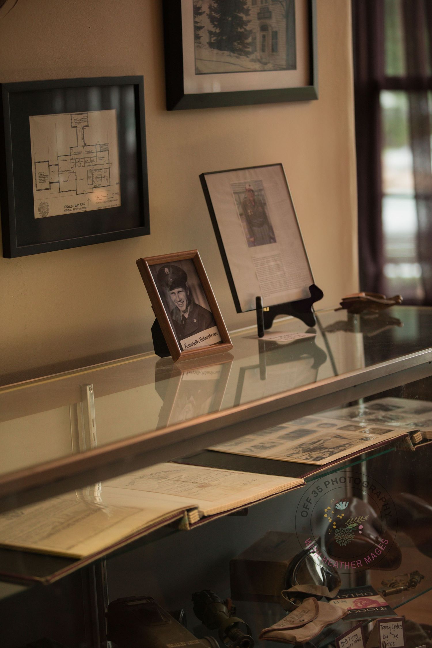 Display case containing historical documents and artifacts with framed photographs on the wall.