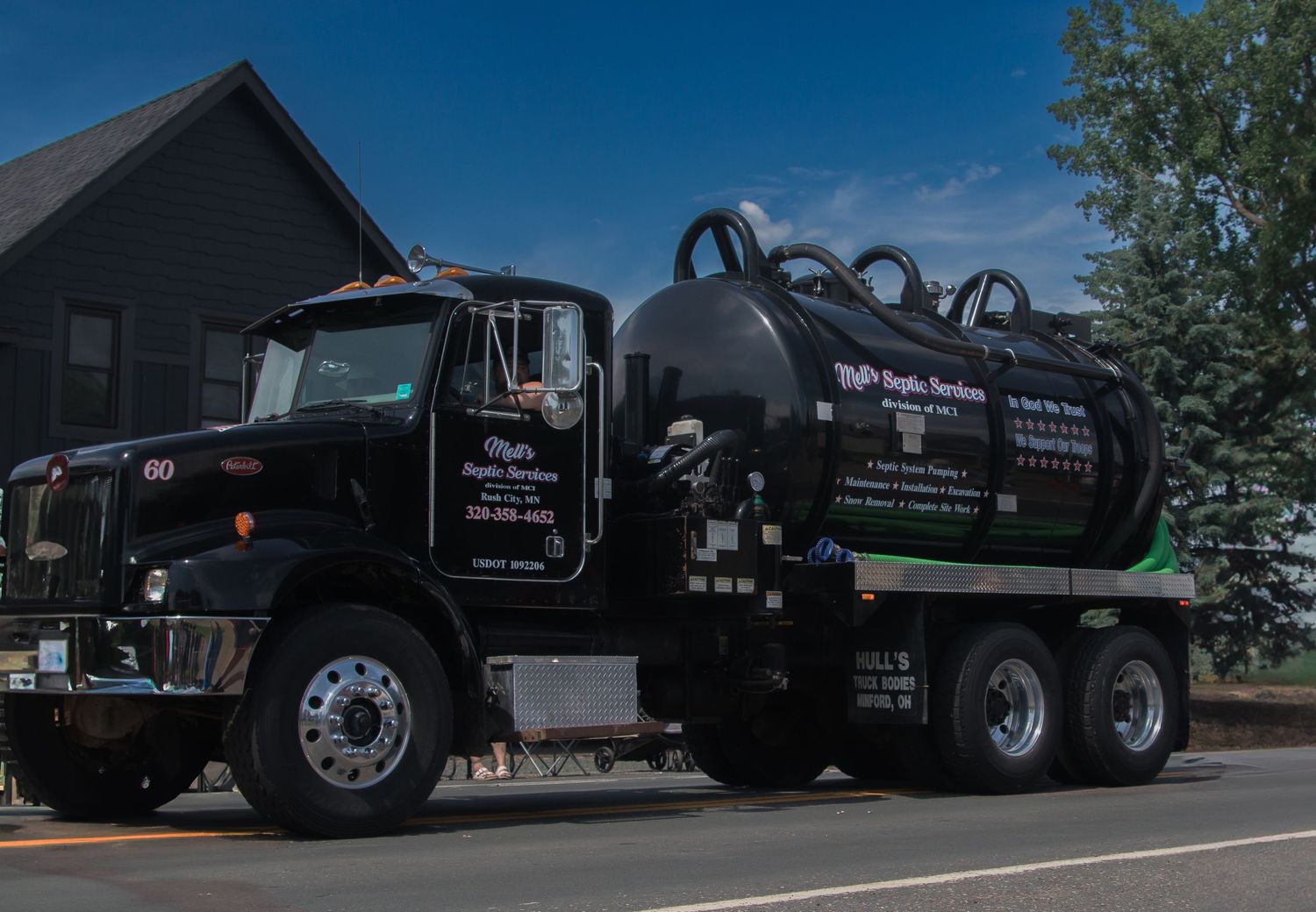 A large black septic tank truck parked in front of trees and buildings.