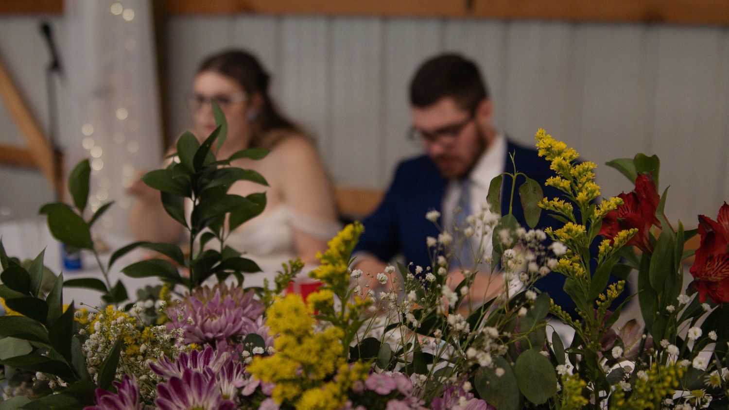 Wedding guests celebrate at reception dining tables adorned with vibrant floral centerpieces and candles.