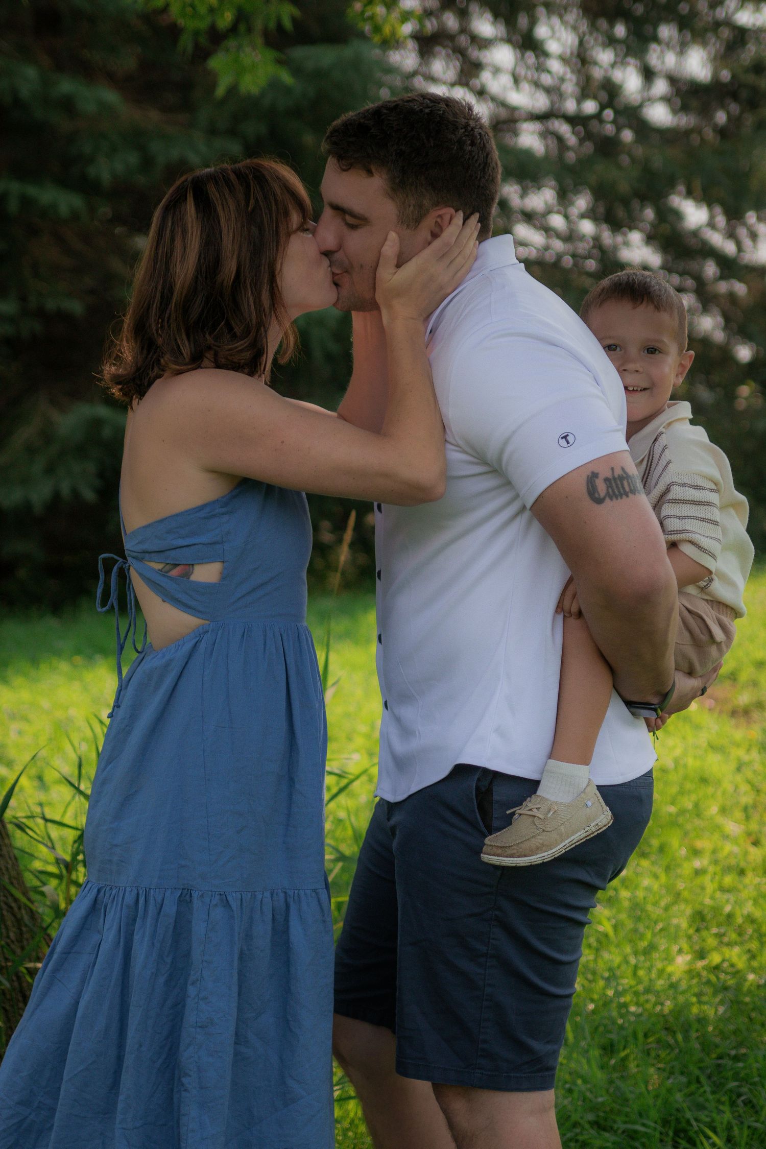 Family sharing an intimate moment together outdoors under green trees.