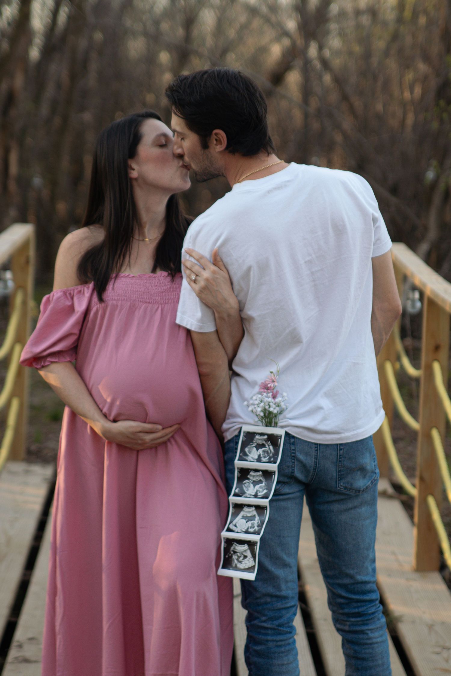 A couple holding a sonogram photo embraces outdoors in a romantic pregnancy announcement photoshoot.