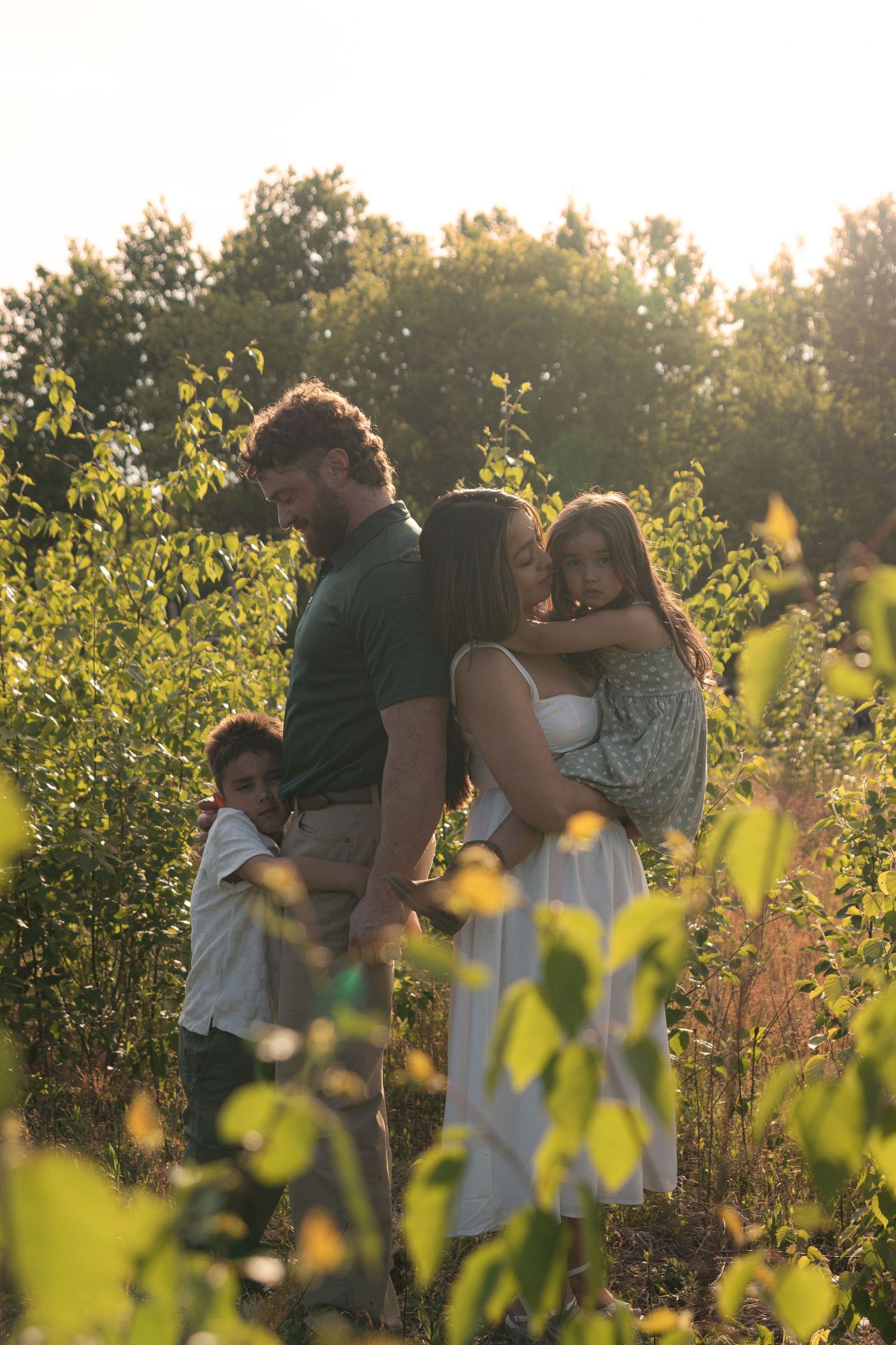 Family embraces in a golden sunlit field of wildflowers during sunset.