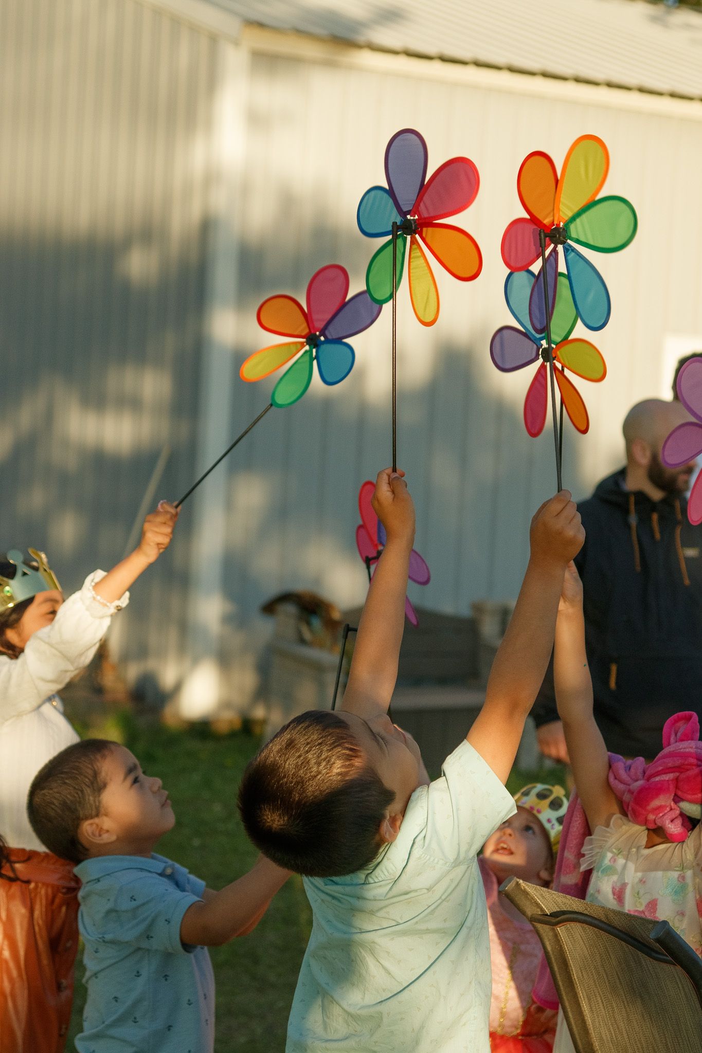 Children reaching up to grab colorful pinwheel spinners in a sunny outdoor setting.