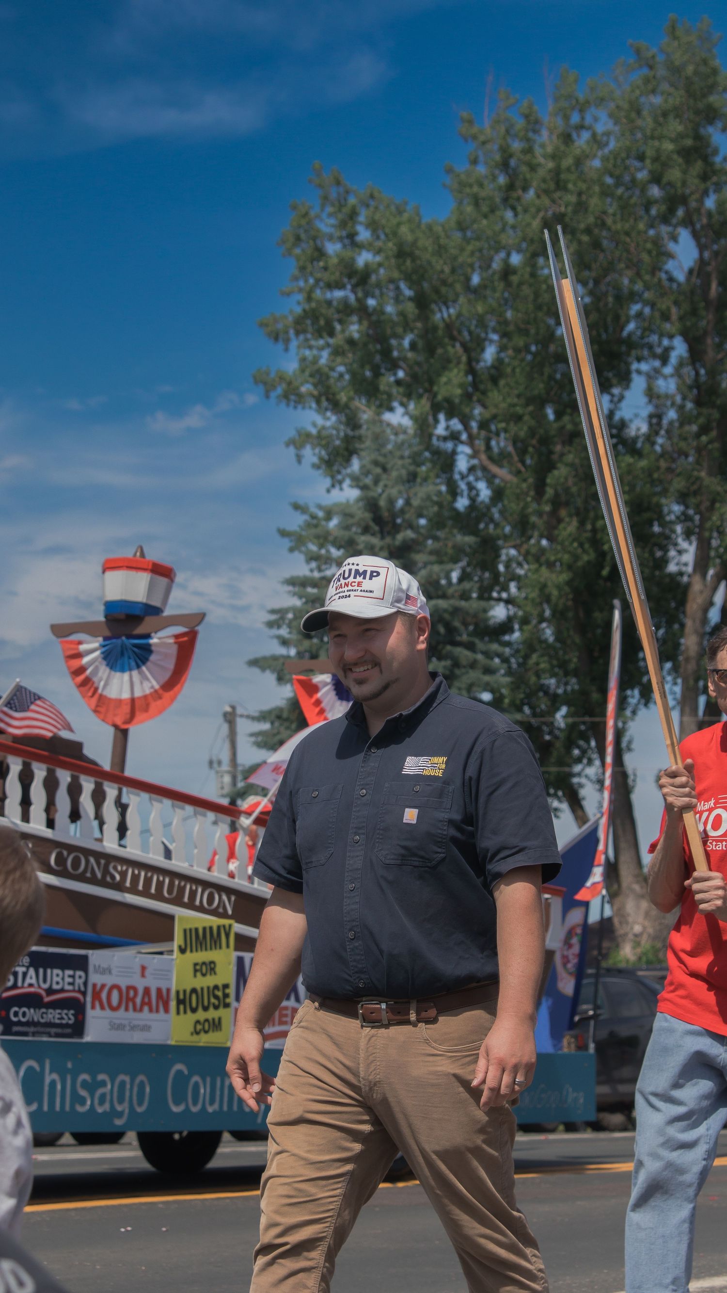 A parade float with patriotic decorations and banners moves down a street during a summer celebration.