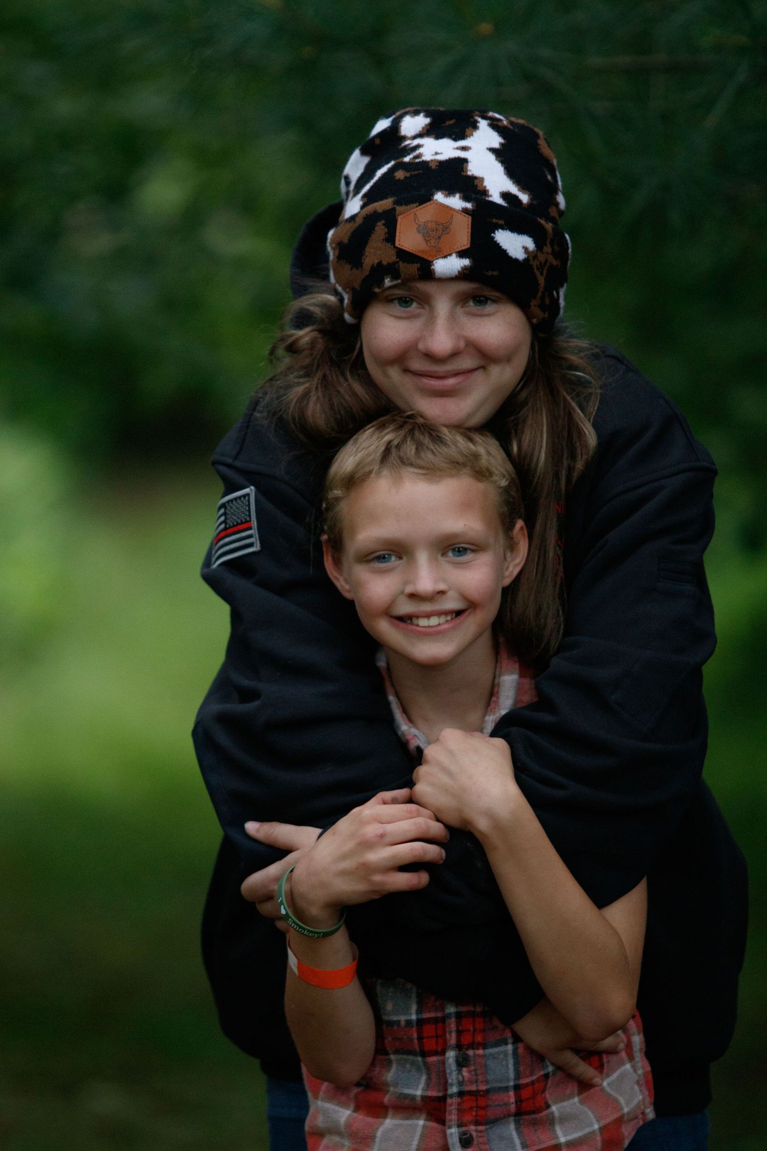 Two people in black and plaid clothing share a playful embrace outdoors in a natural setting.