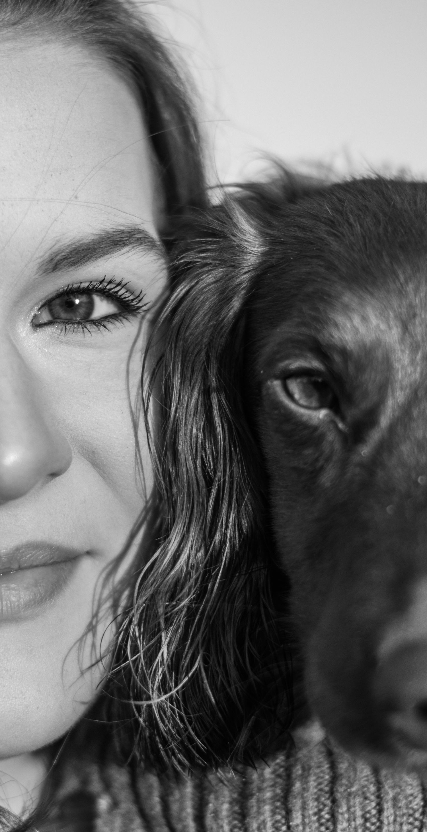 Black and white close-up portrait of a young woman and dark Labrador dog side by side, sharing a tender moment.