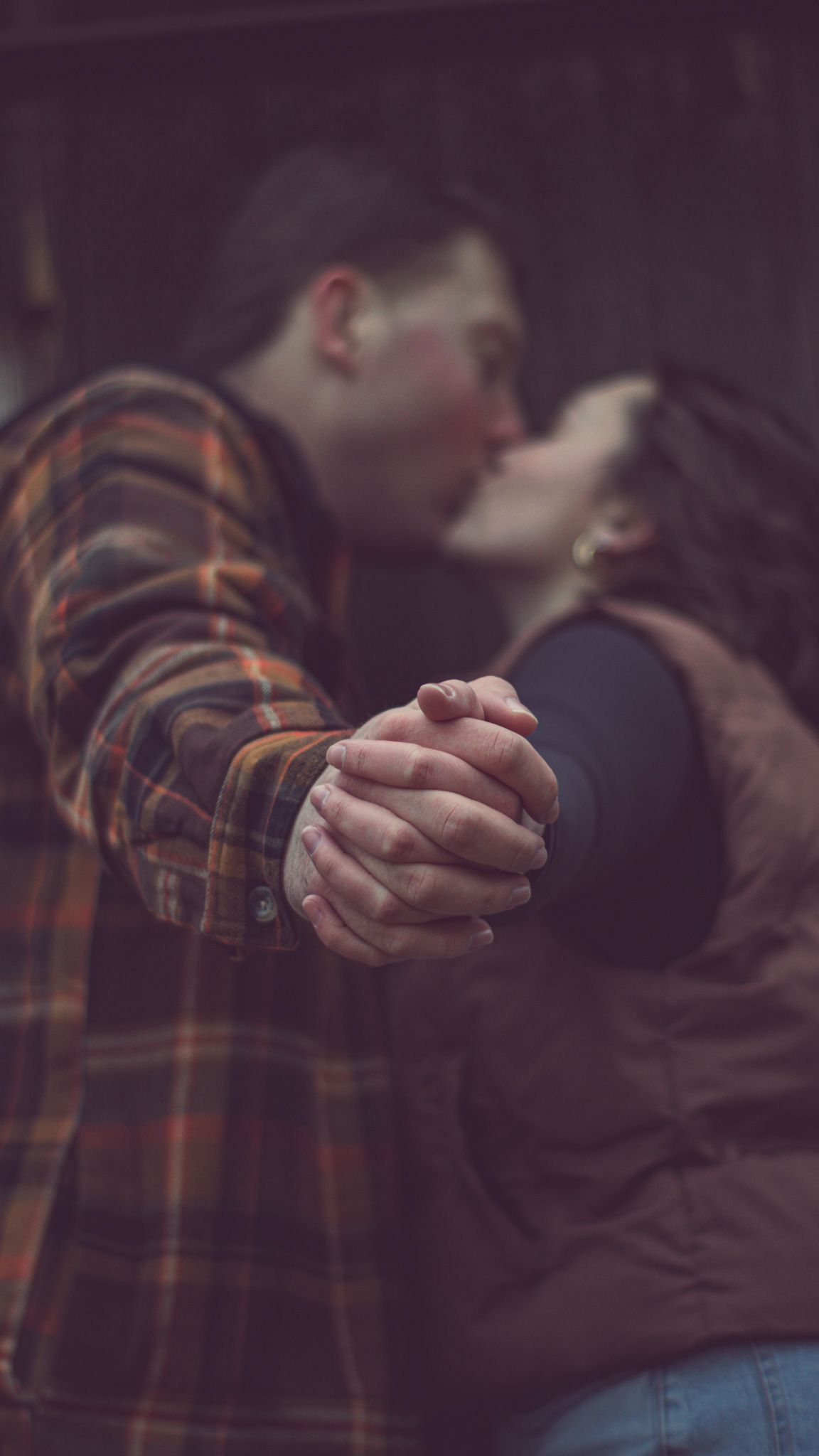 A couple holds hands intimately while sharing a romantic moment with interlocked fingers in soft lighting.