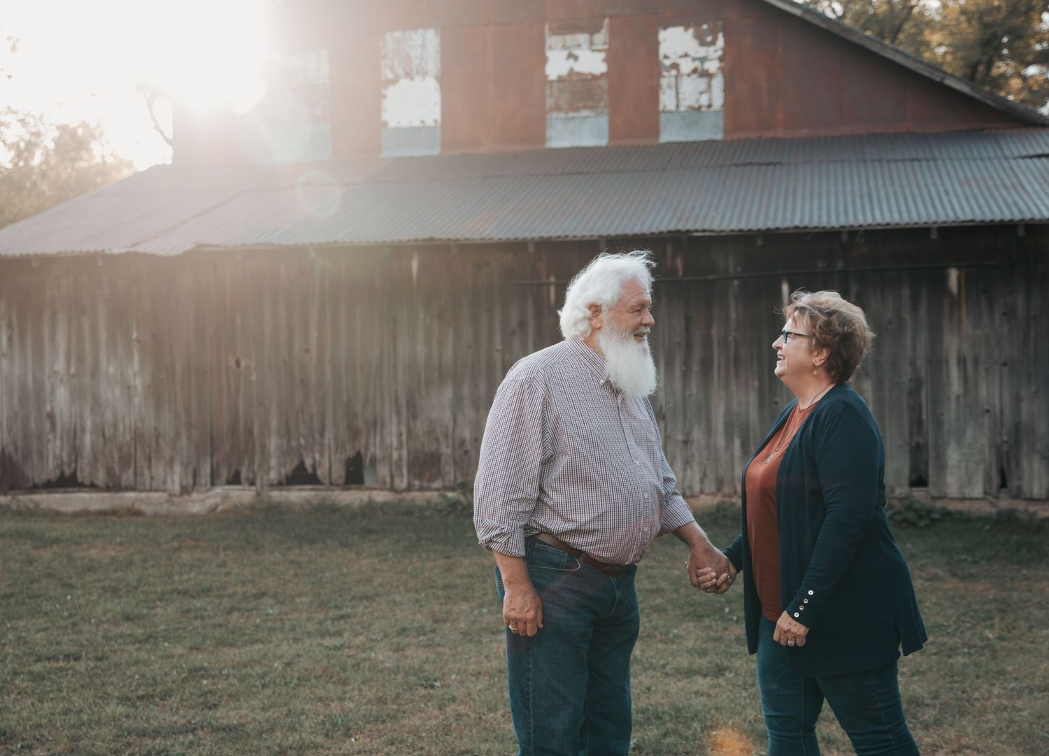 Elderly couple walking together through a sunlit backyard at golden hour with lens flare in the background.
