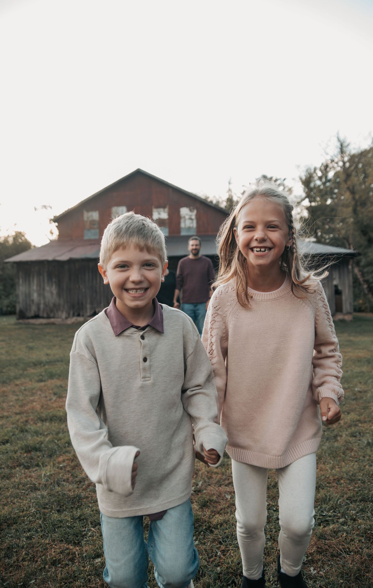 Two young children in casual sweaters and jeans playing together outdoors on a grassy field.