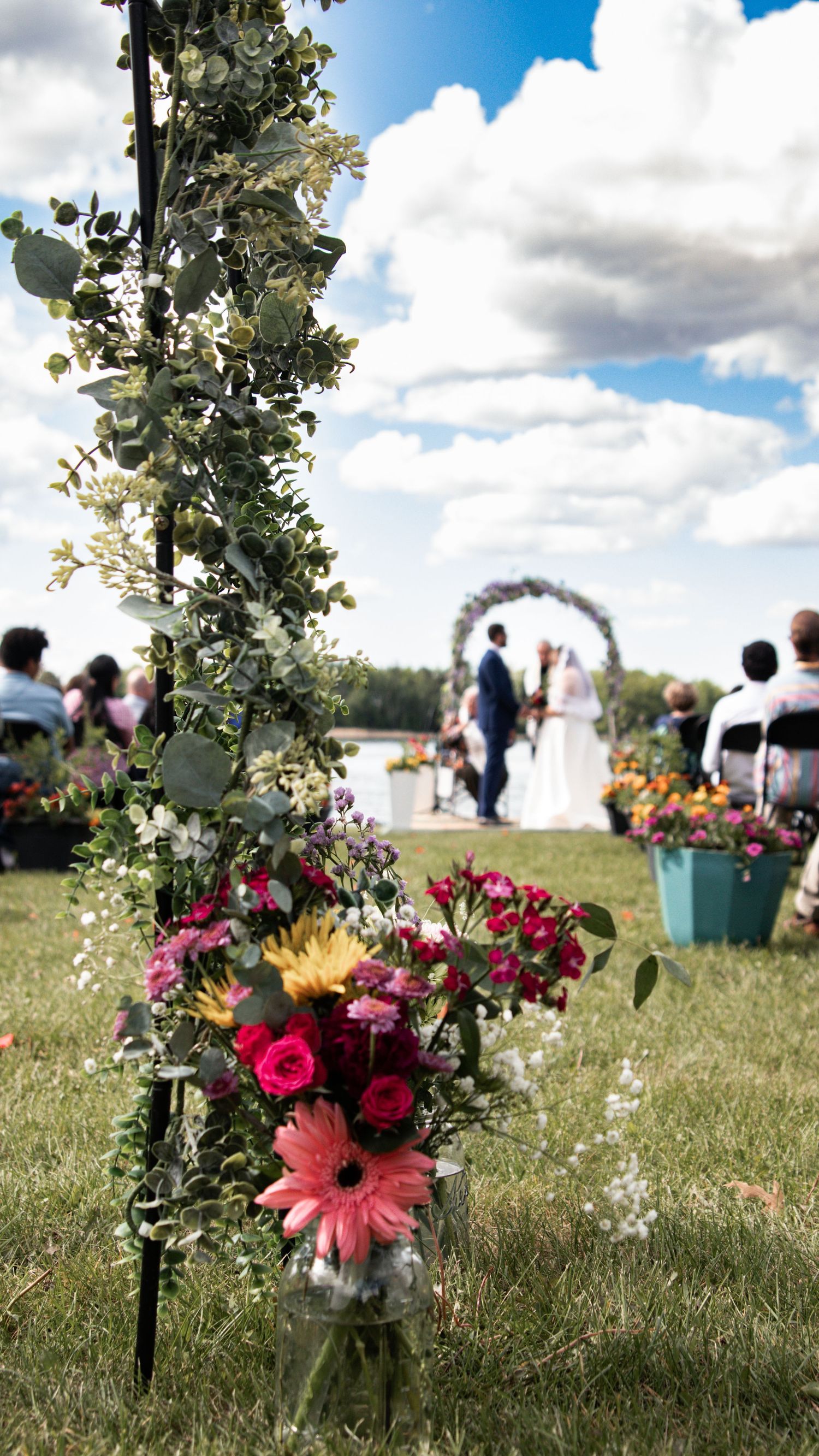 Beautiful floral wedding arch and decorations set up in a sunny meadow with white wildflowers and pink roses.
