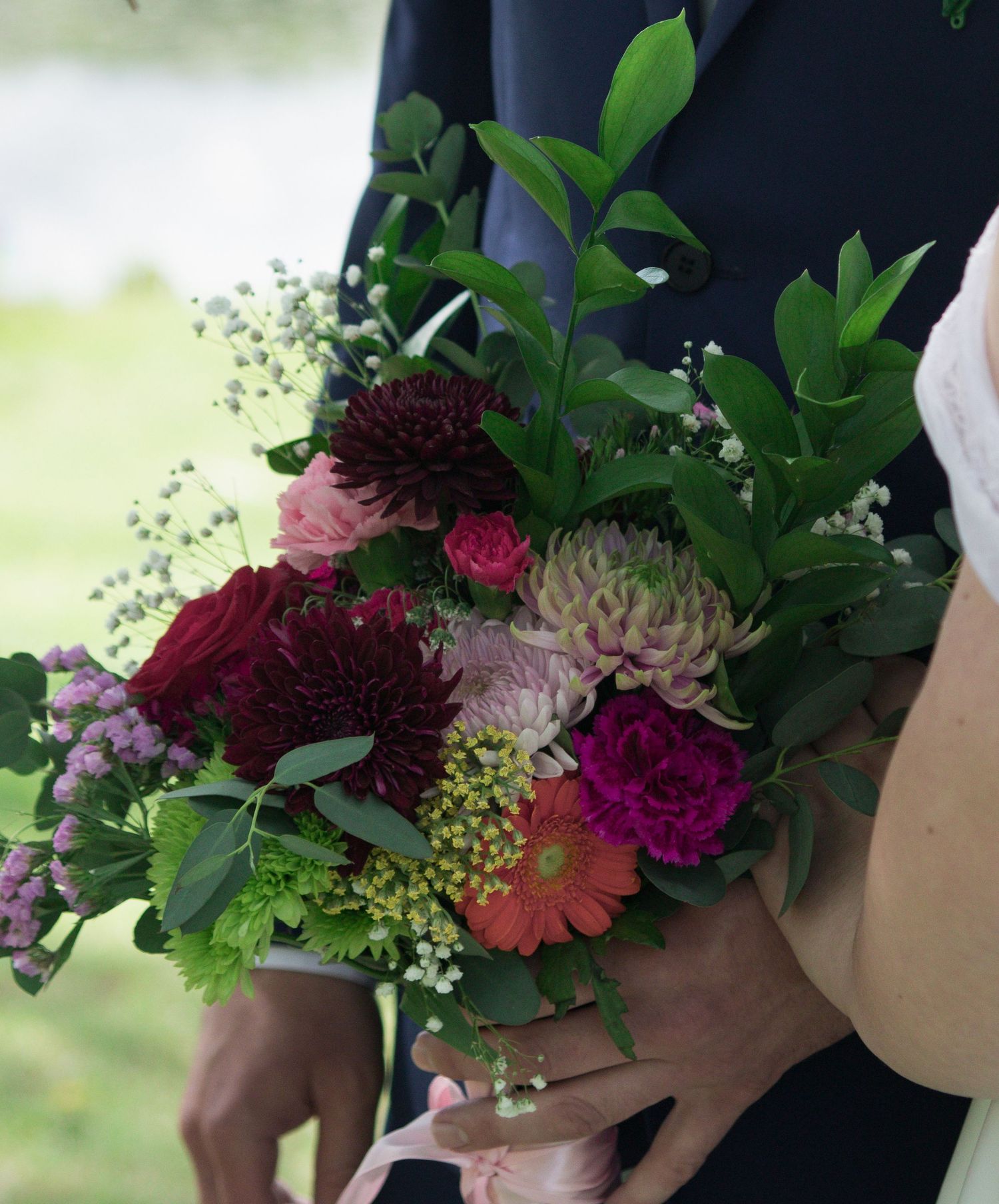 An elegant wedding bouquet featuring deep burgundy and pink flowers with lush greenery and delicate foliage.