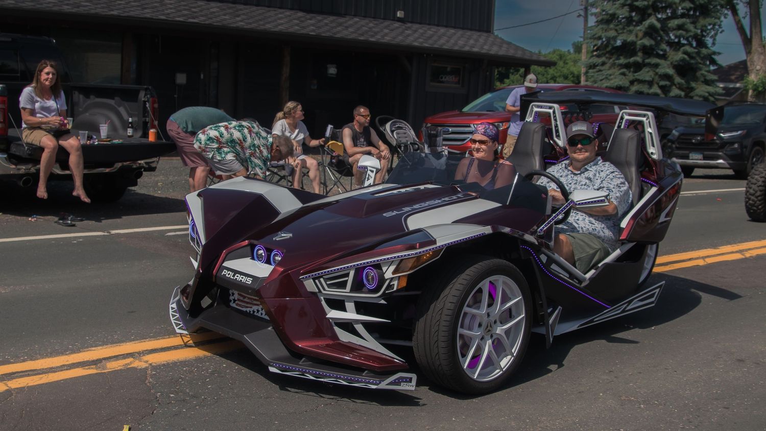 Purple luxury vehicles displayed at an outdoor car show with spectators viewing.