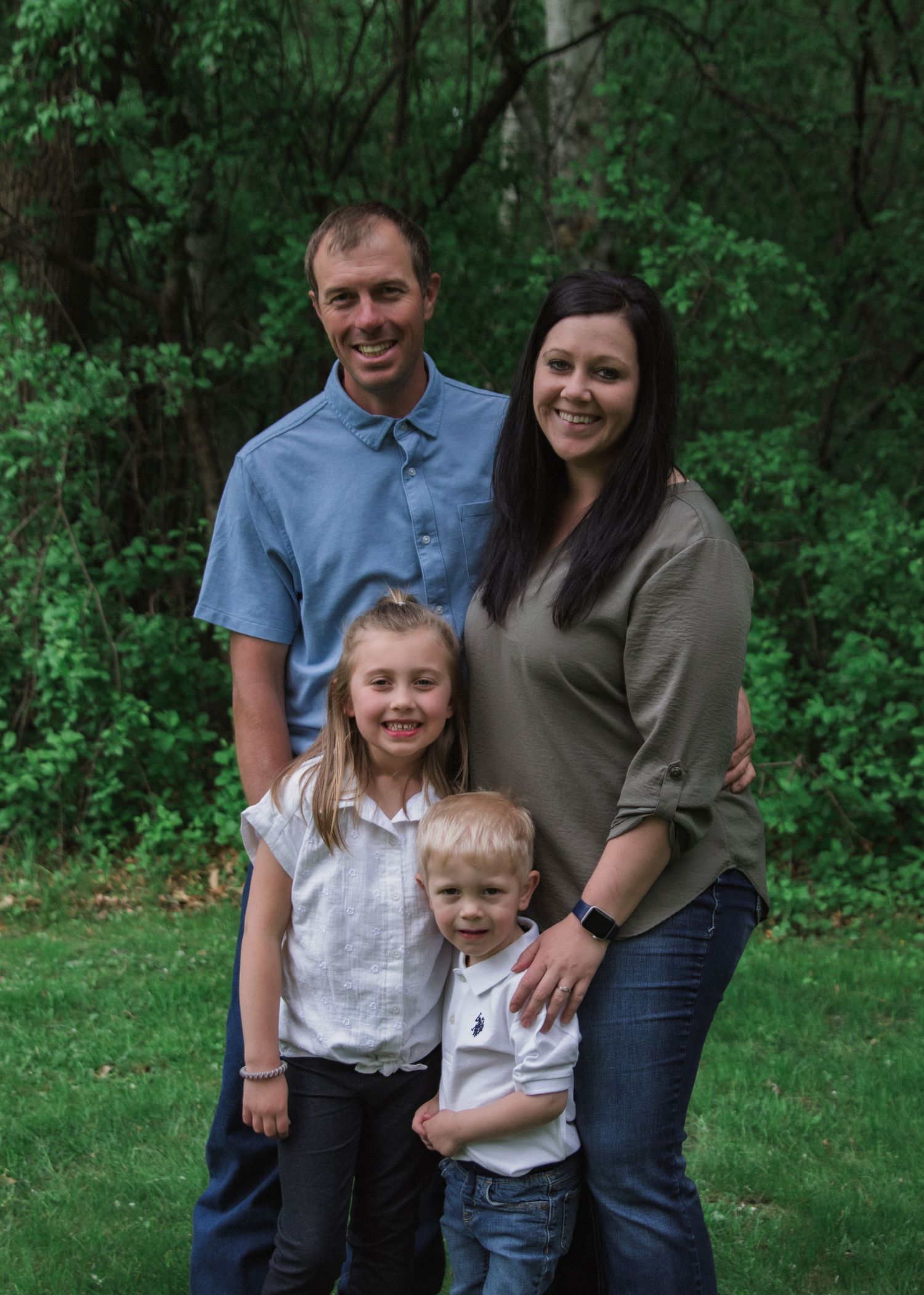 Family members posing together against a backdrop of green trees and foliage.
