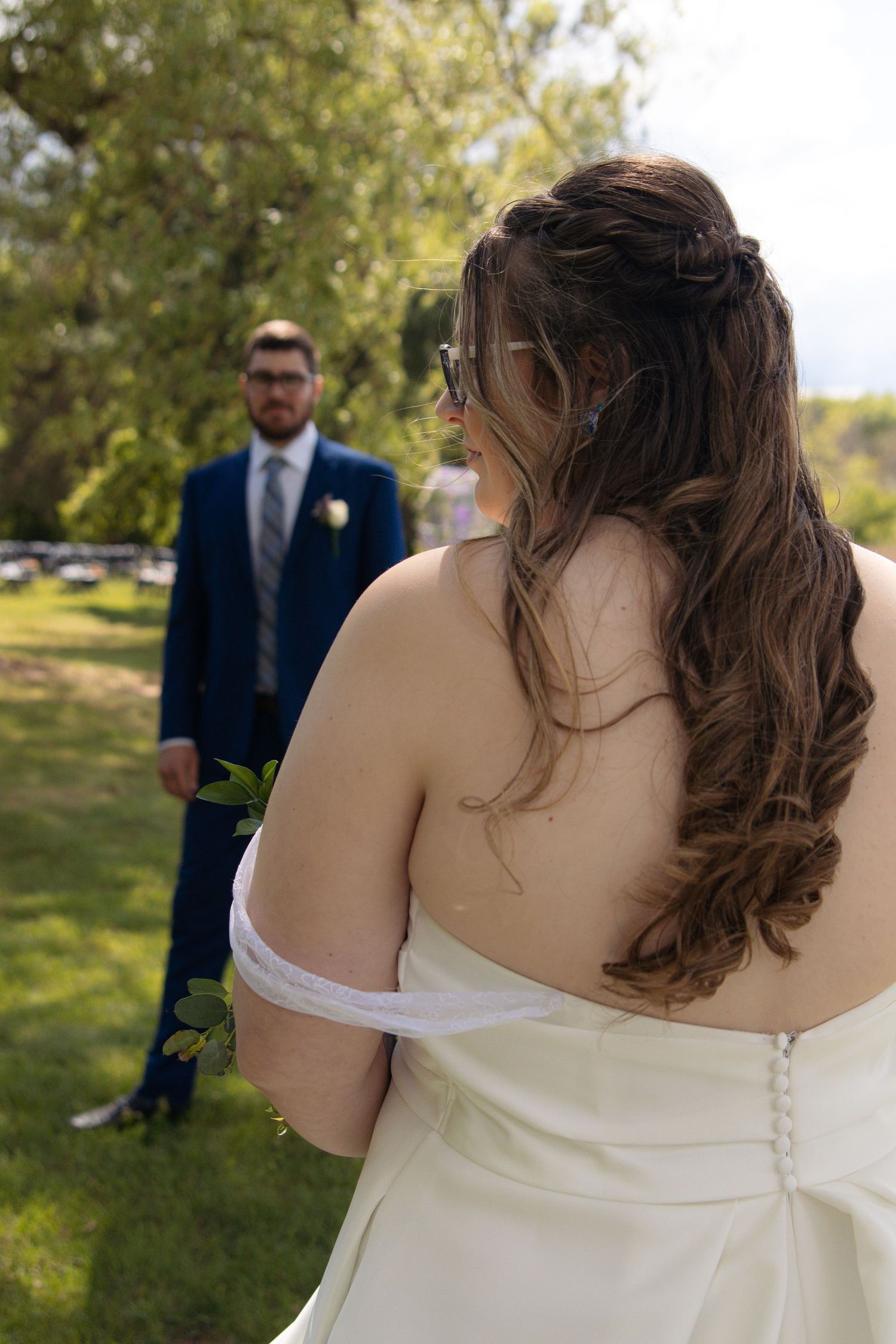 A wedding couple in an outdoor garden setting with the bride in a white dress and flowing brown hair in the foreground.