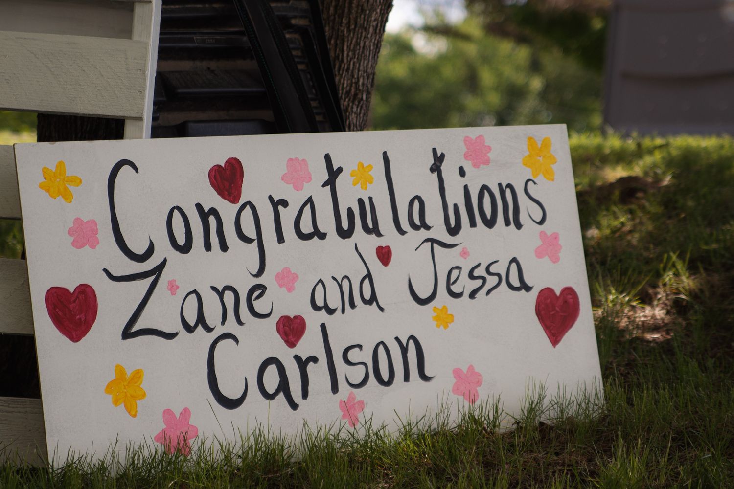 White congratulatory wedding signs decorated with hearts and stars displayed outdoors in a garden setting.