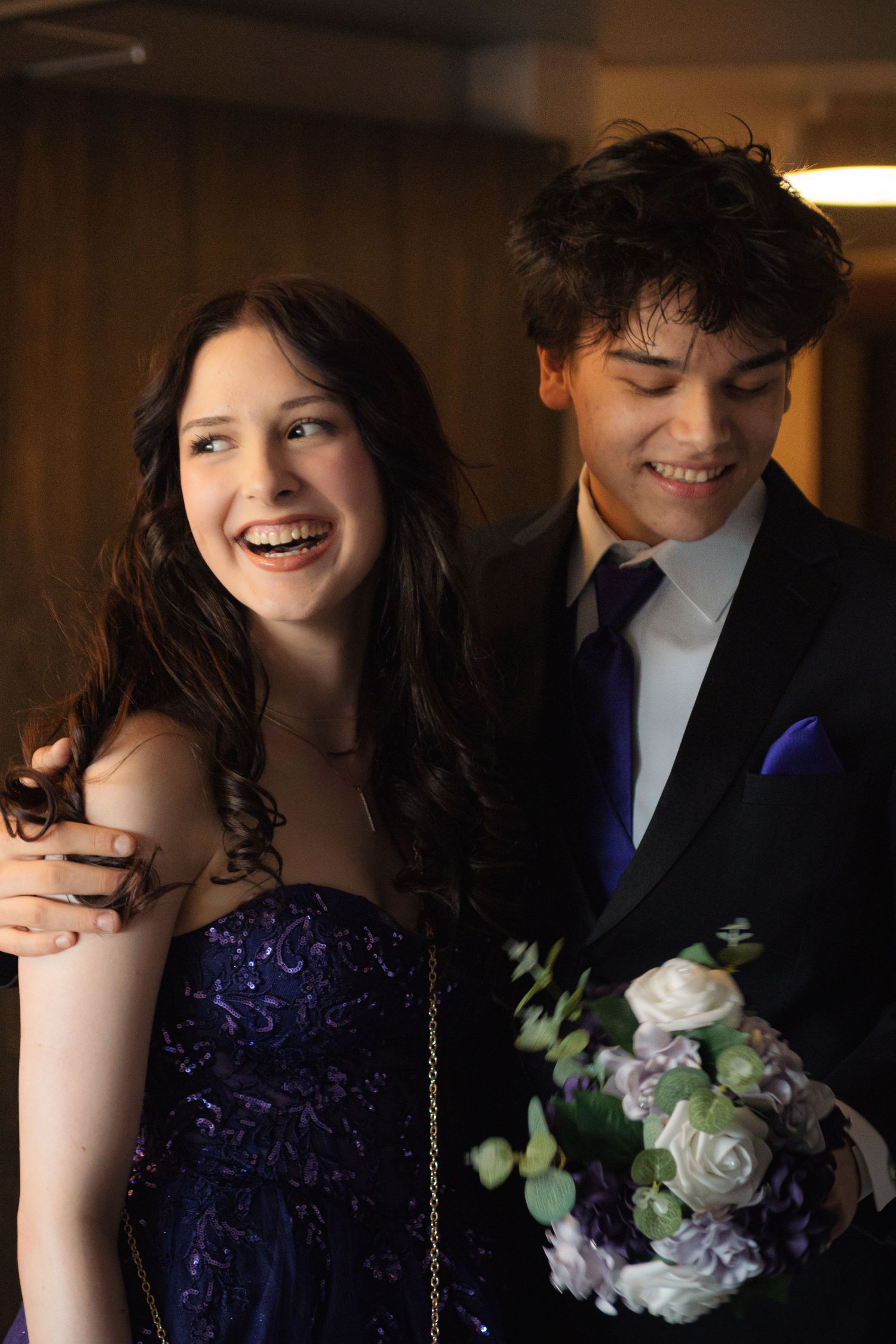 A couple in formal attire sharing a joyful moment with a white rose bouquet.