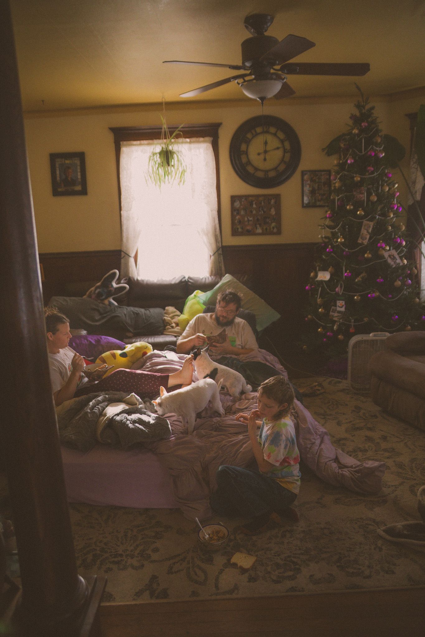Children relaxing in a cozy living room with a decorated Christmas tree, ceiling fan, and warm holiday atmosphere.