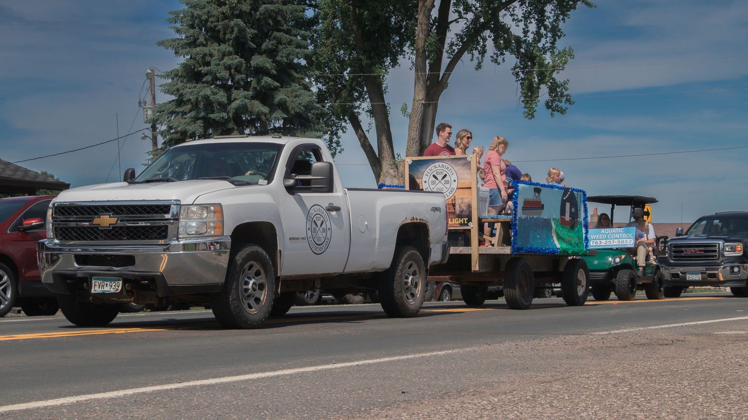 A white pickup truck leads a parade of decorated floats down a street.